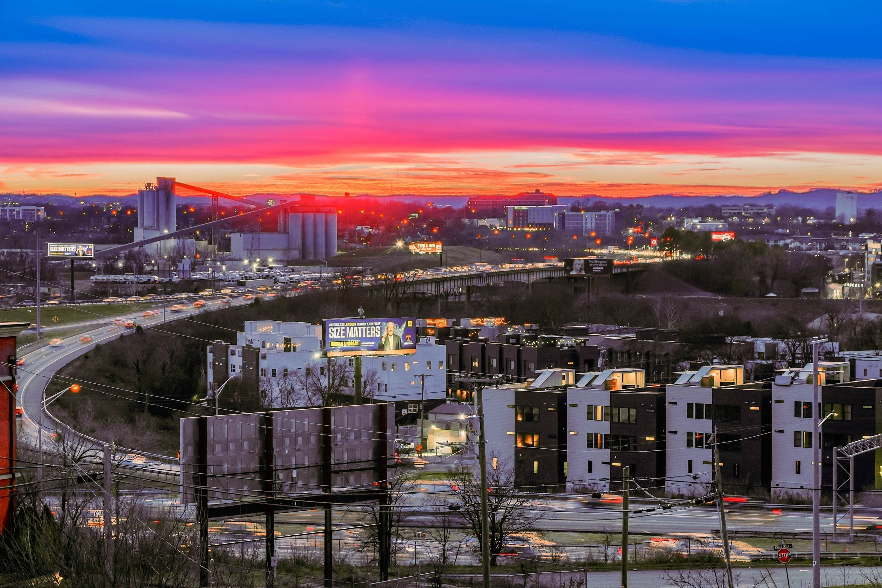 A cityscape at dusk with a bridge, modern buildings, and a highway.