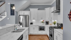 A modern kitchen with white cabinetry, stainless steel appliances, and a wooden floor. - Game Room Balcony Backyard Near Downtown Nash (Nashville)