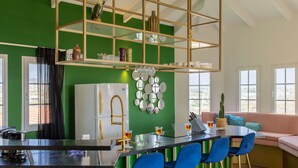 Eine moderne Küche mit grüner Akzentwand, einer Bar mit blauen Stühlen und einer Sitzecke mit einer Couch und einer Kakteenpflanze.