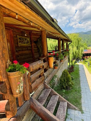 A rustic wooden cabin with a porch, potted plants, and a view of the surrounding landscape.