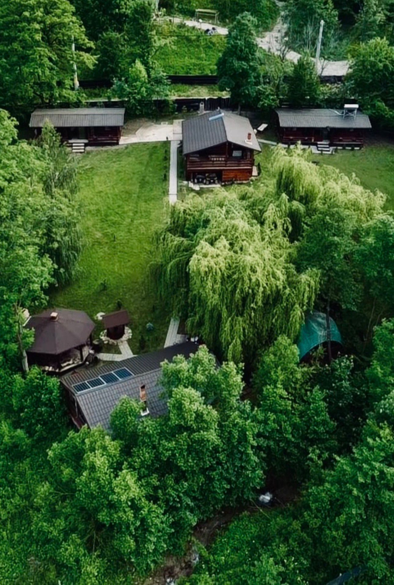 Ett stort hus omgivet av frodig grönska, med en liten lusthus och en täckt uteplats.