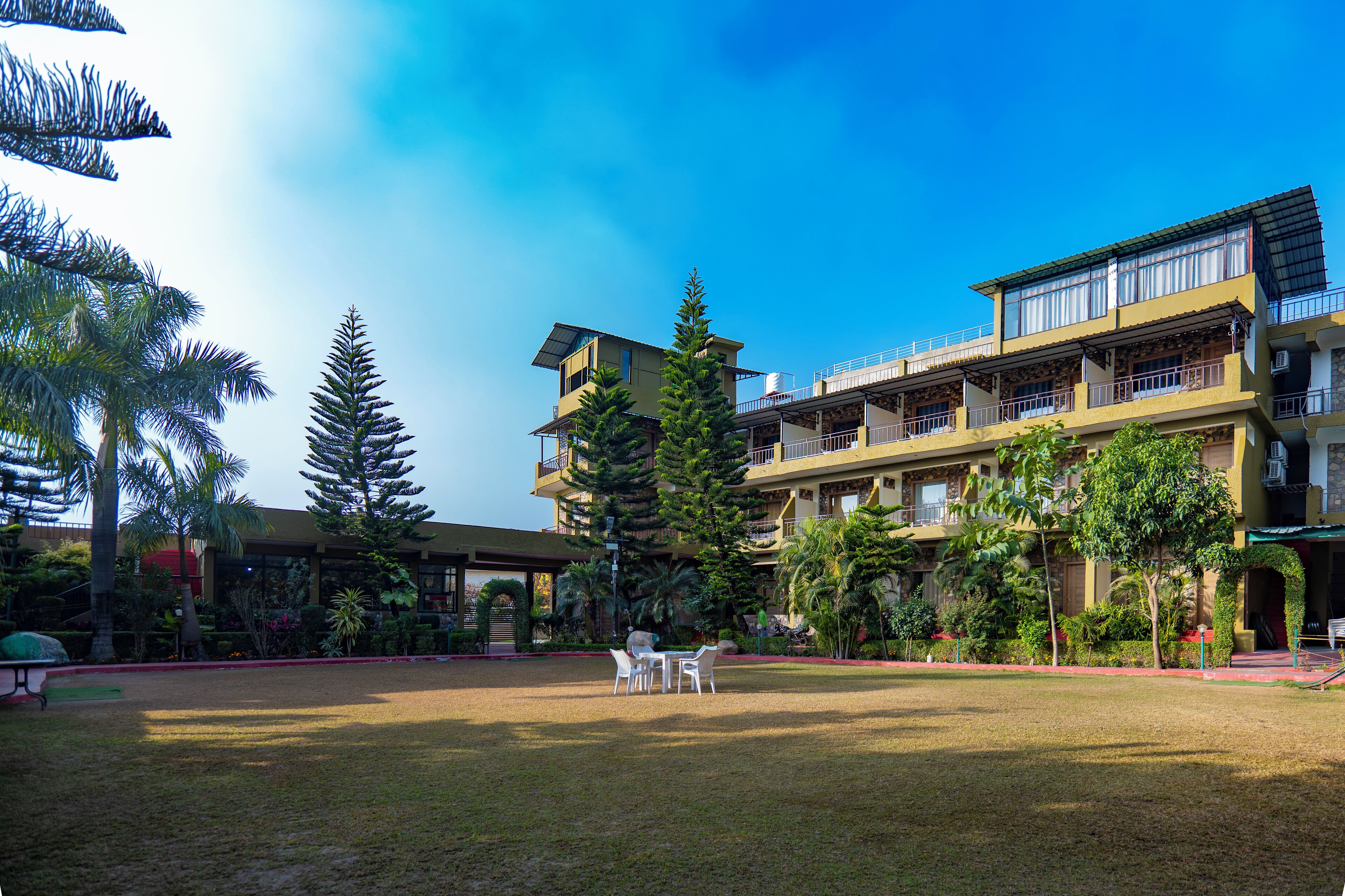 A hotel courtyard with outdoor seating, surrounded by lush greenery and a multi-story building with balconies.