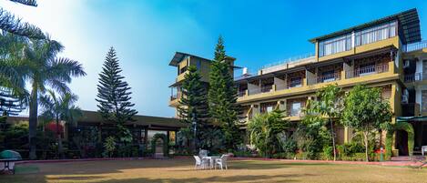 A hotel courtyard with outdoor seating, surrounded by lush greenery and a multi-story building with balconies.