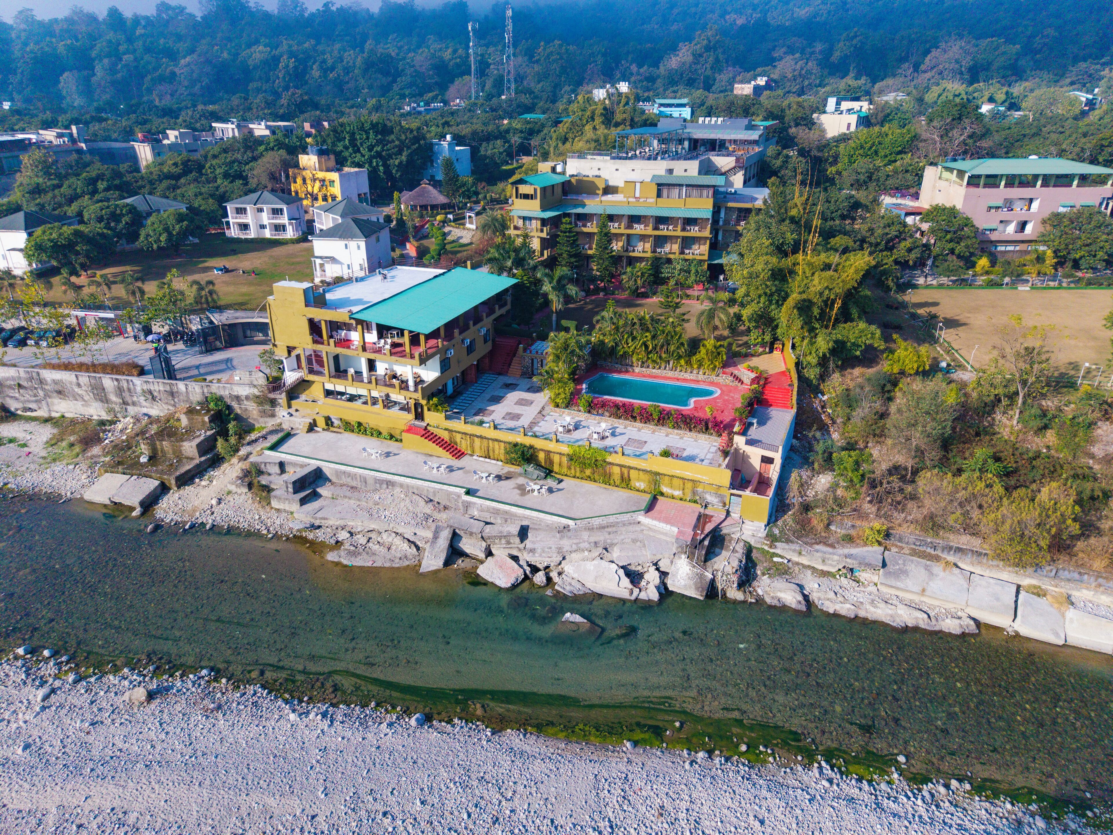 An aerial view of a resort with a swimming pool, multiple buildings, and a rocky shoreline.