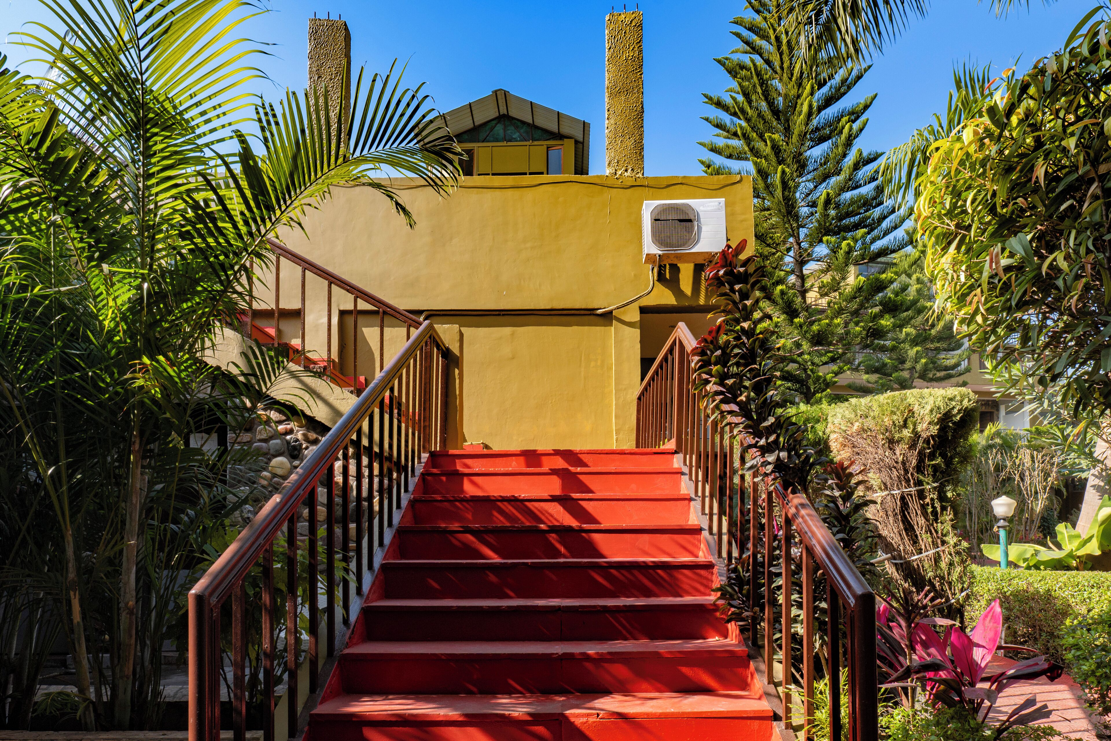 A red staircase leading to a building with an air conditioning unit on the wall.