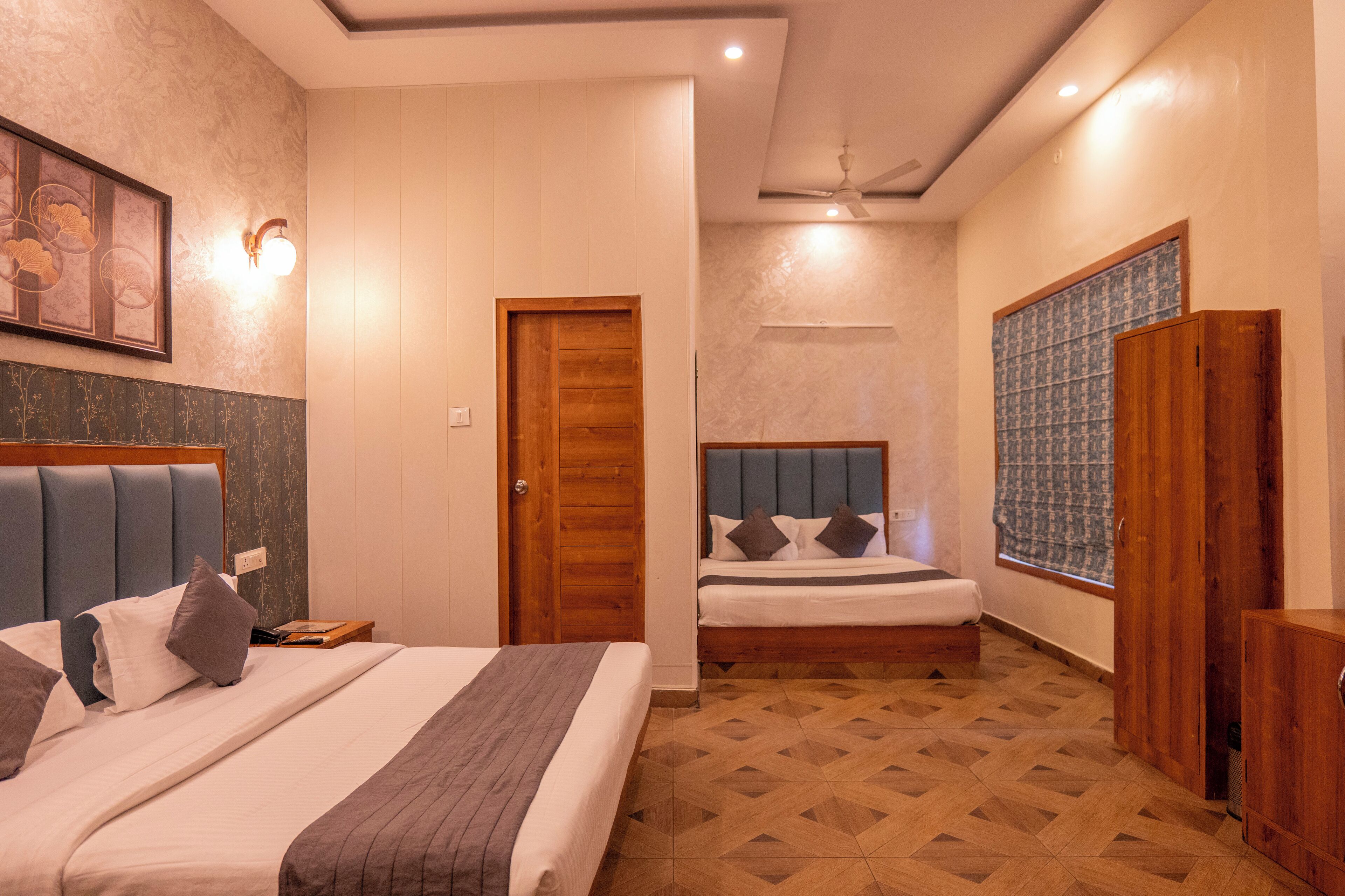 Une chambre d’hôtel avec deux lits, une porte en bois, un ventilateur de plafond et un papier peint à motifs.