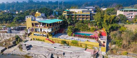 A multi-story hotel with a pool, located near a river.