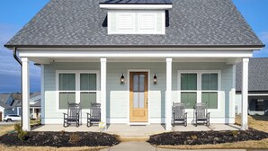 Une maison à deux étages avec un porche à l’avant, une porte centrale et deux fenêtres de chaque côté.