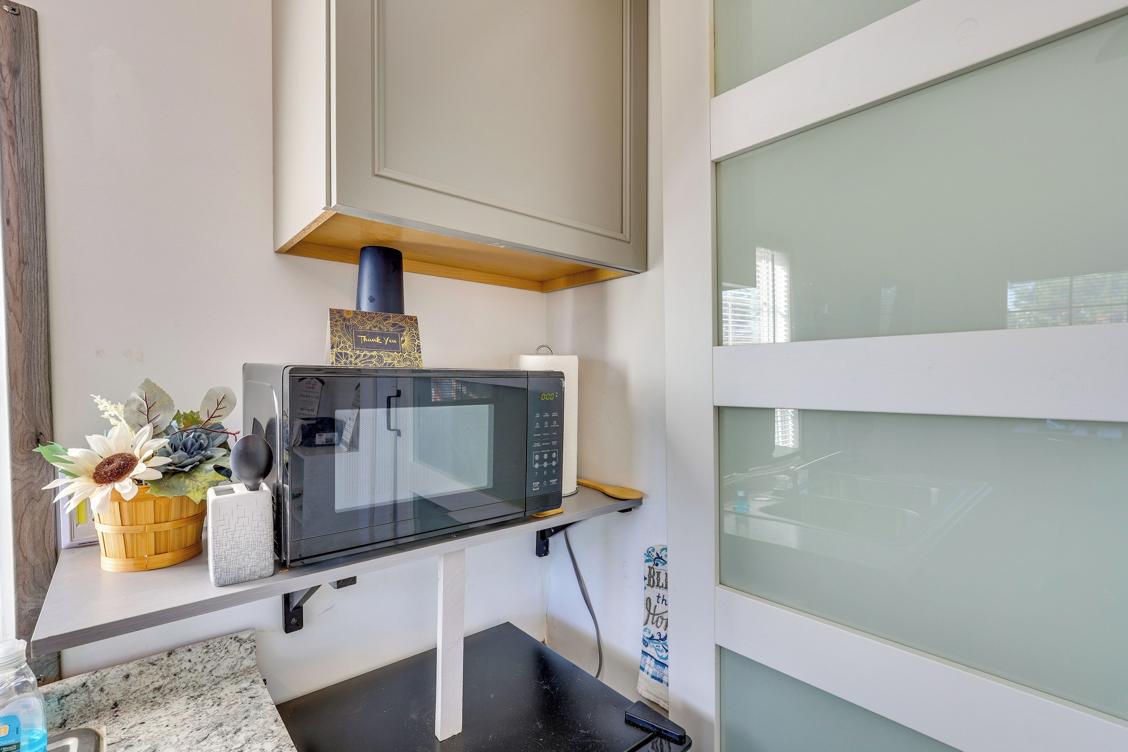 A kitchen with a microwave on a countertop, a wooden basket with flowers, and a towel hanging on the wall.