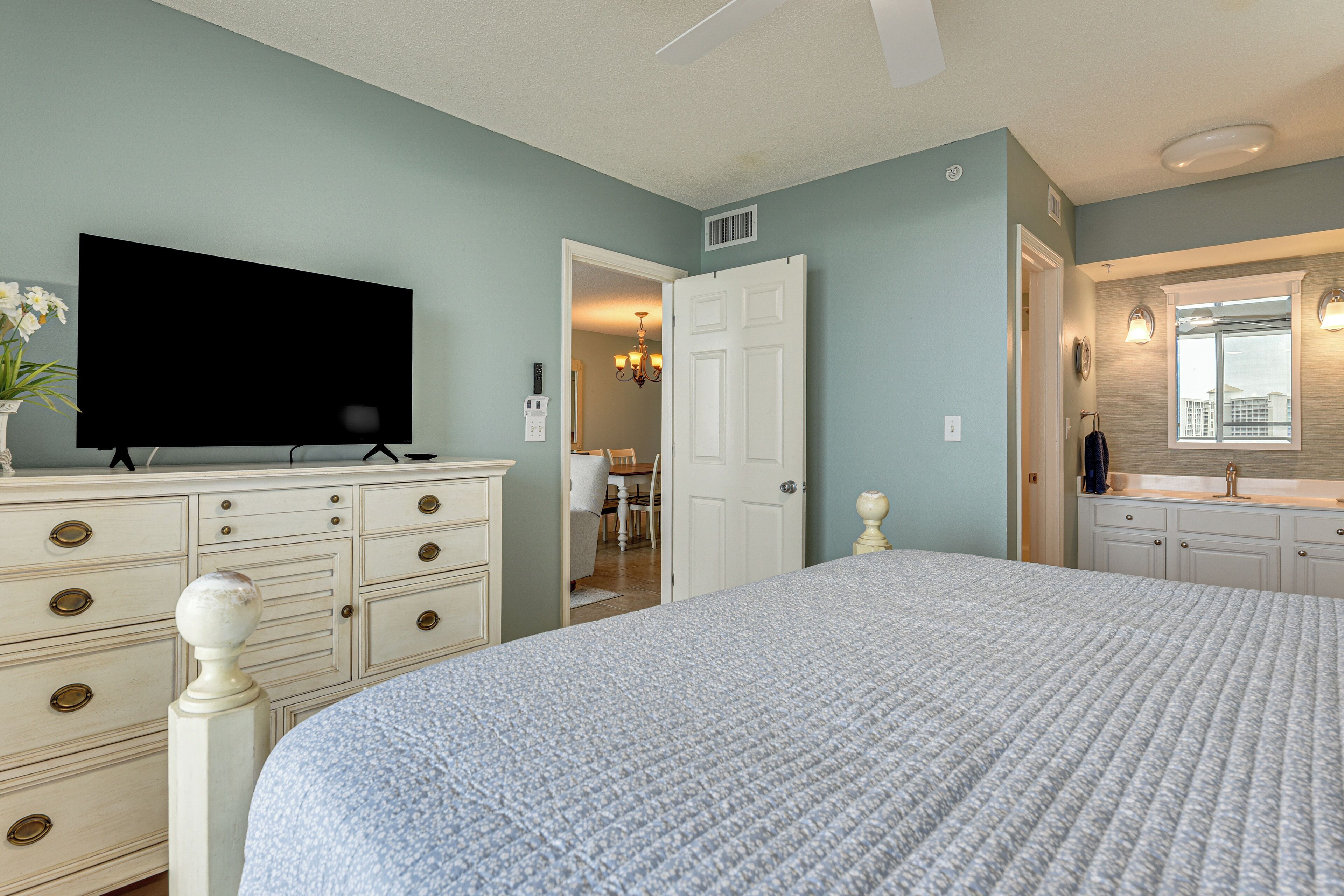 Une chambre à coucher avec un grand lit, une commode, un téléviseur et une salle de bain équipée d’un miroir et d’un lavabo.