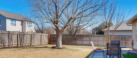 A backyard with a wooden fence, a tree, and a patio with chairs and a table.