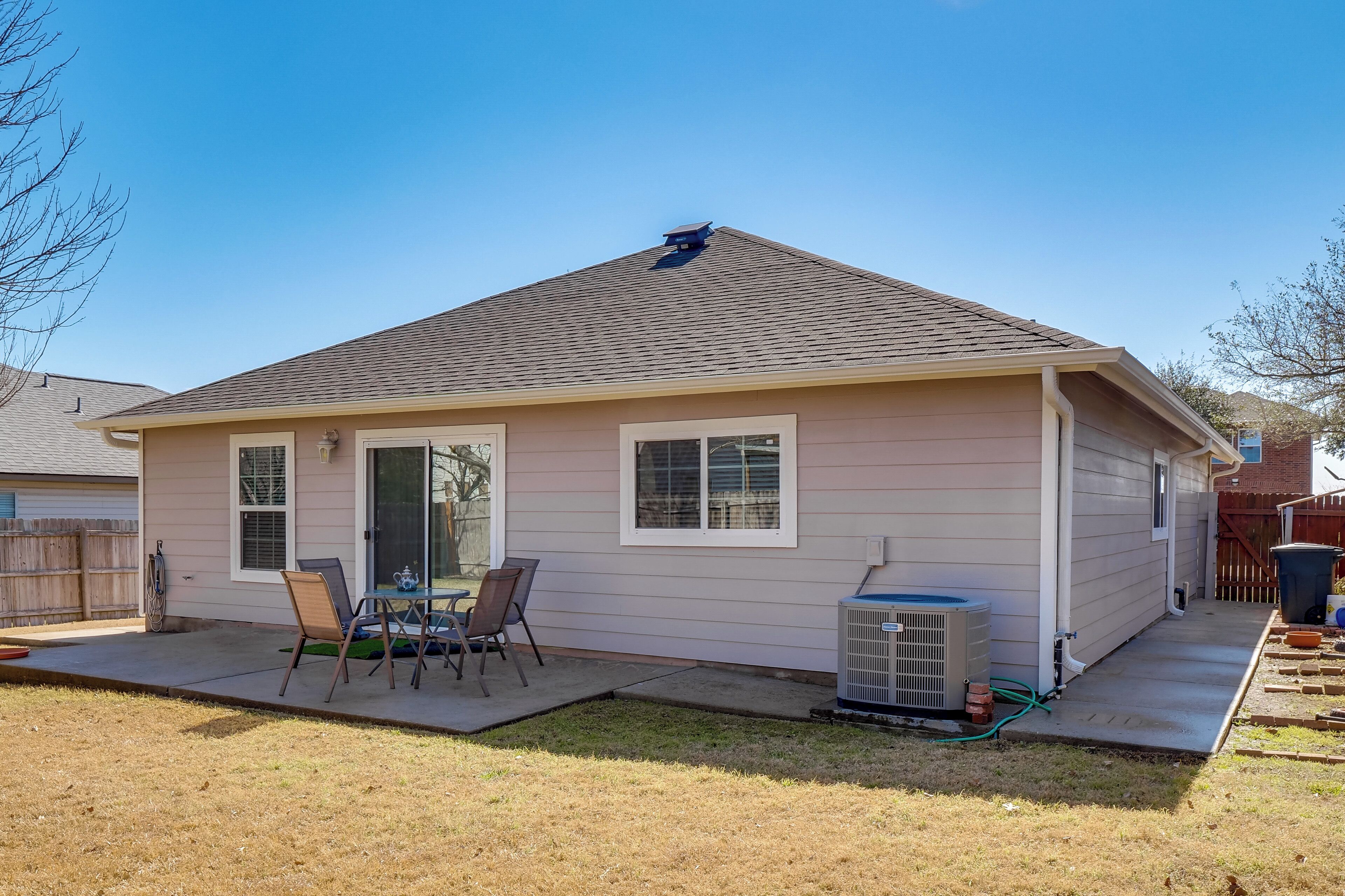 A single-story house with a covered patio, a small table and chairs, and an air conditioning unit.