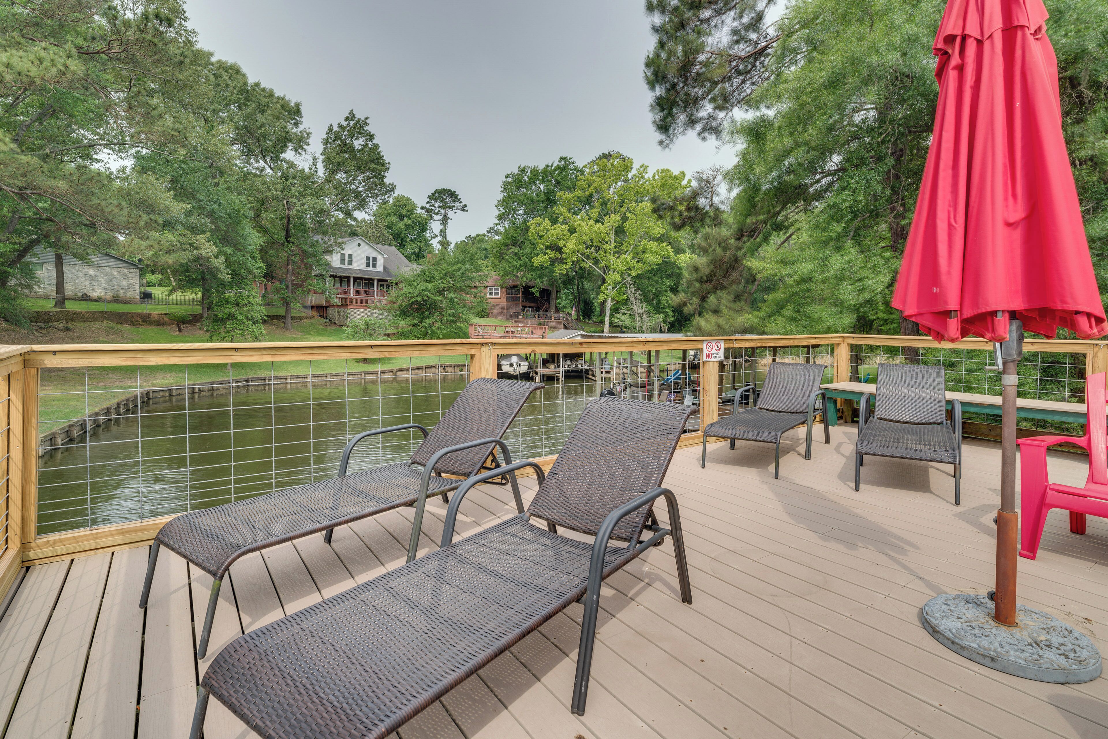 A deck with chairs and tables overlooking a body of water, surrounded by trees and buildings.