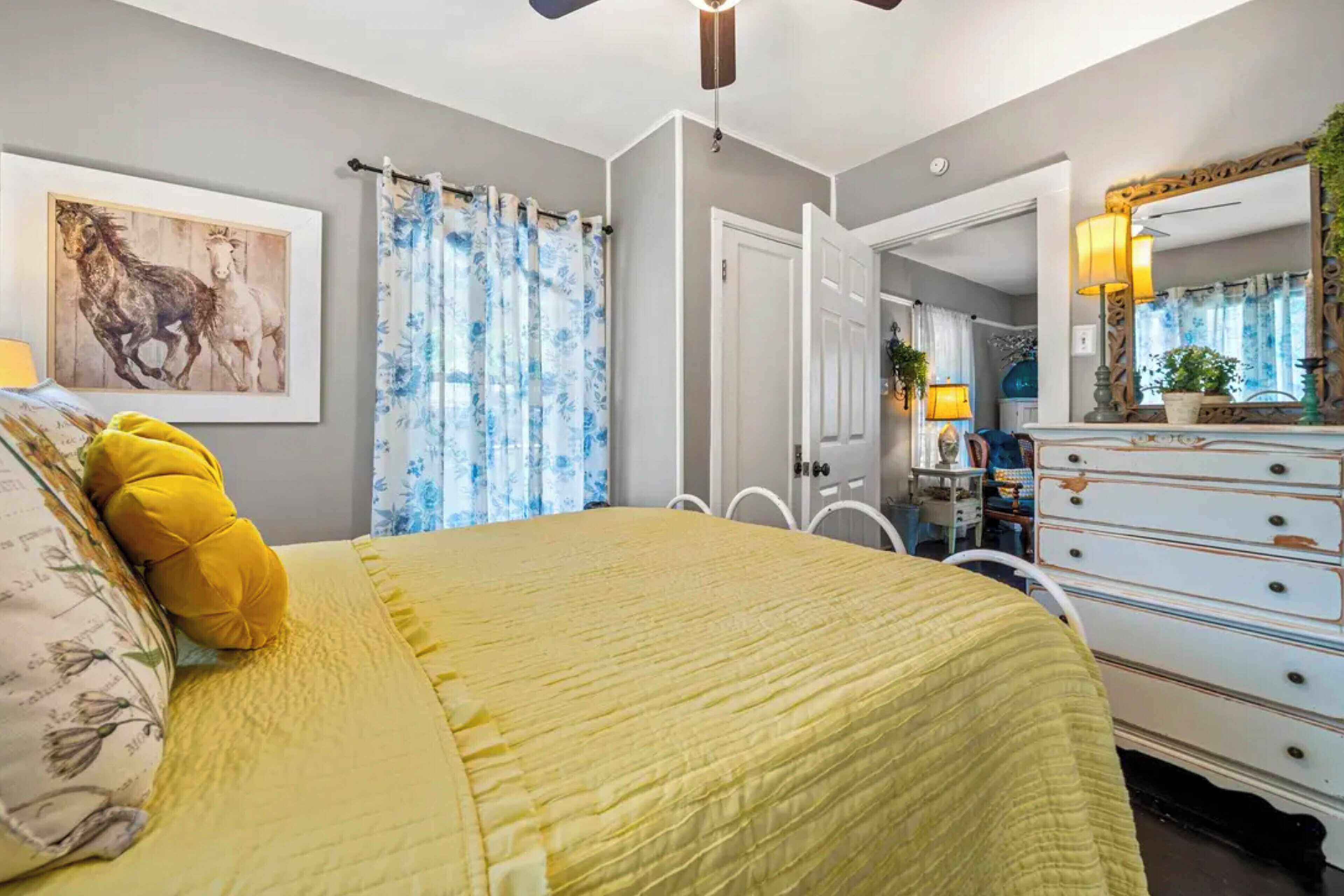 Une chambre à coucher comprenant un lit, une commode, un miroir et une porte donnant sur une autre pièce.