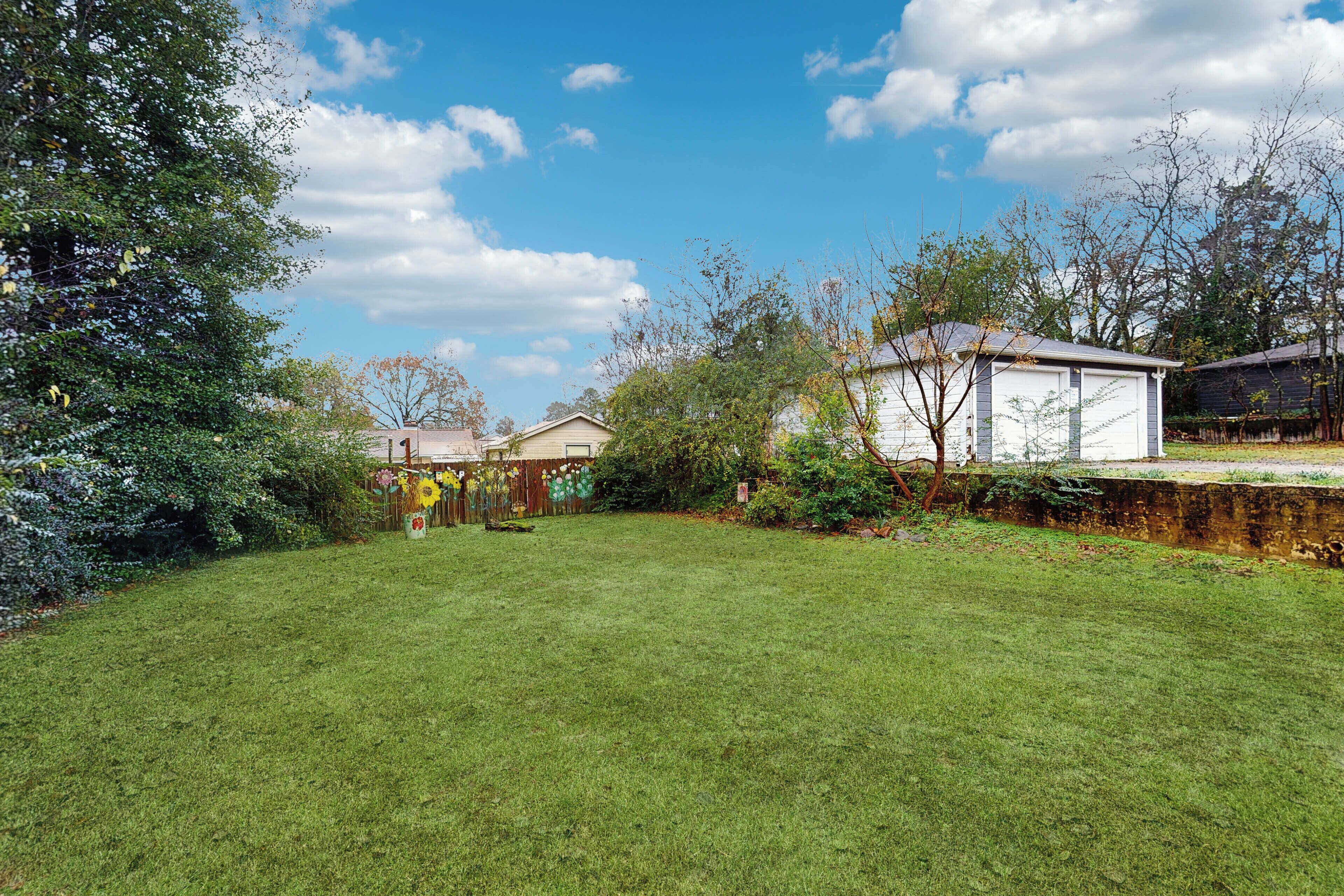 A residential backyard with a lawn, a garage, and a house with a sloped roof.