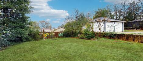 A residential backyard with a lawn, a garage, and a house with a sloped roof.