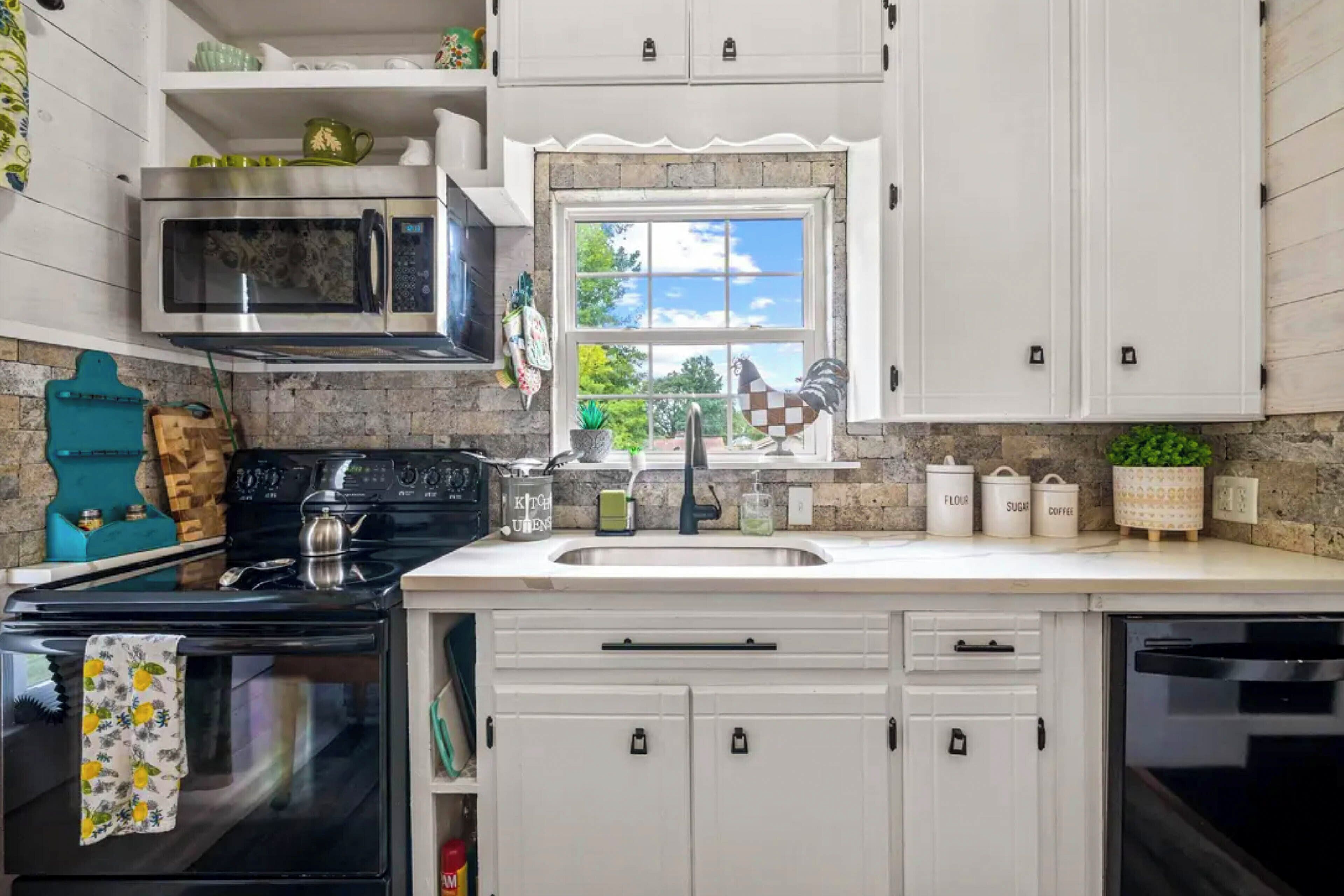 A kitchen with white cabinets, a microwave, a stove, and a window with a view of greenery.