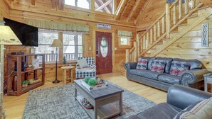 A cozy cabin interior with a wooden staircase, a leather sofa, and a television. - Family Haven w/ Hot Tub! 5 Mi to Dtwn Pigeon Forge (Sevierville)