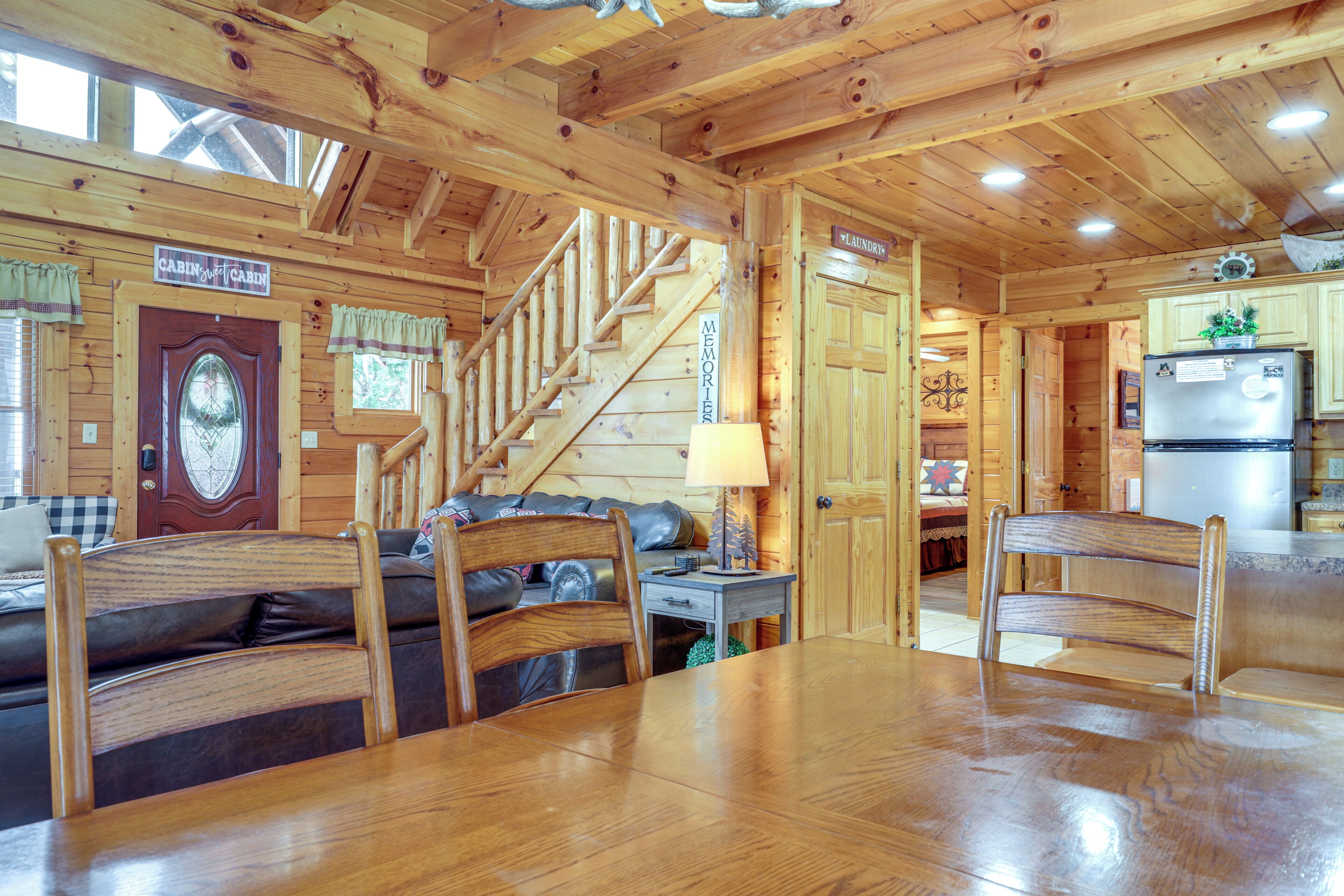 Ein Holzblockhaus-Innenraum mit Esstisch, Stühlen, einer Couch, einer Treppe und einer Küchenzeile.