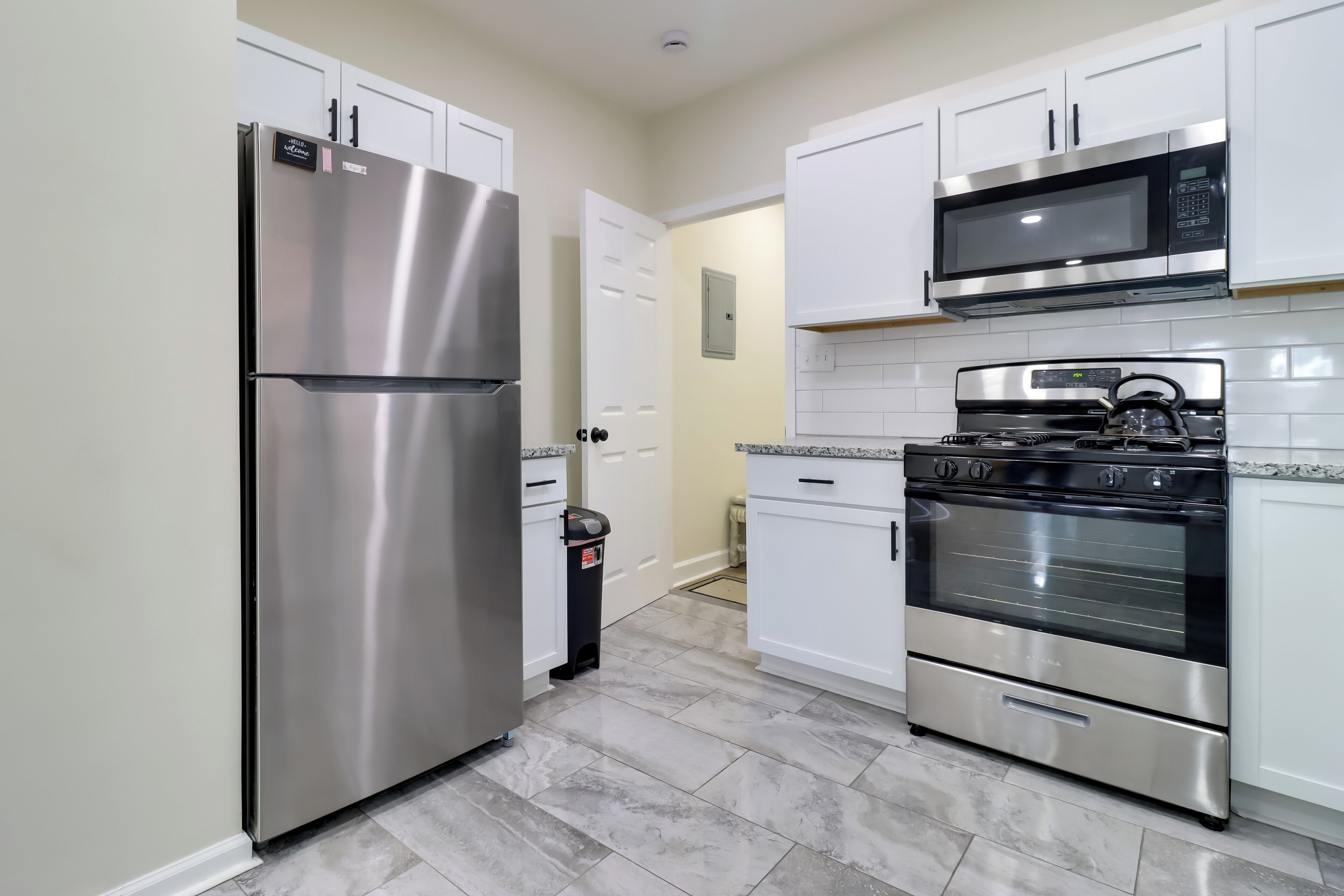A modern kitchen with stainless steel appliances, white cabinets, and a tiled backsplash.
