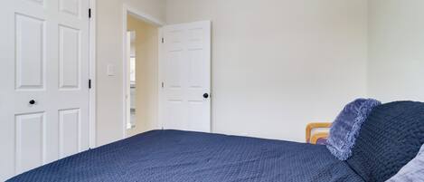 A bedroom with a large bed, two white doors, and a wooden nightstand.
