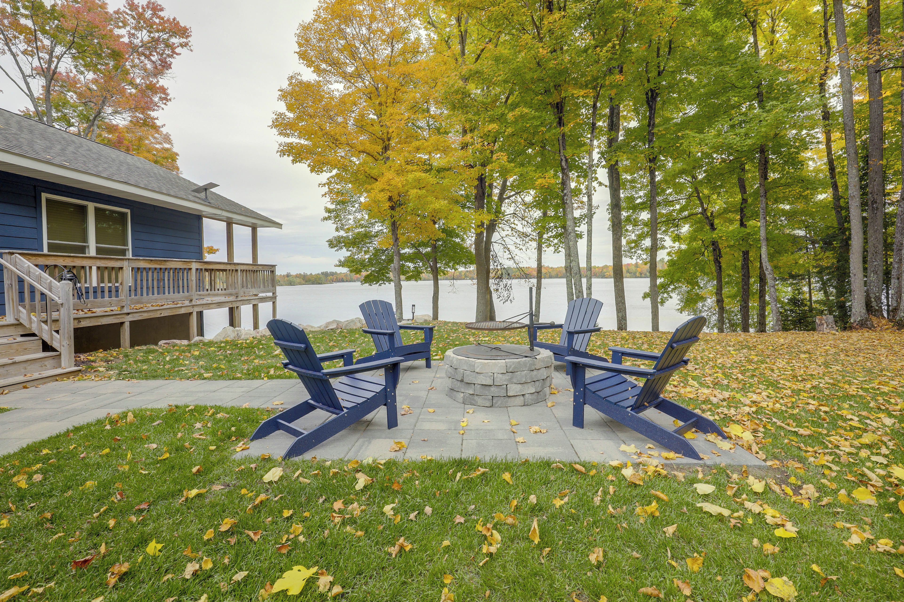 Terraza junto al lago con sillas Adirondack y una hoguera, con vista a un cuerpo de agua.