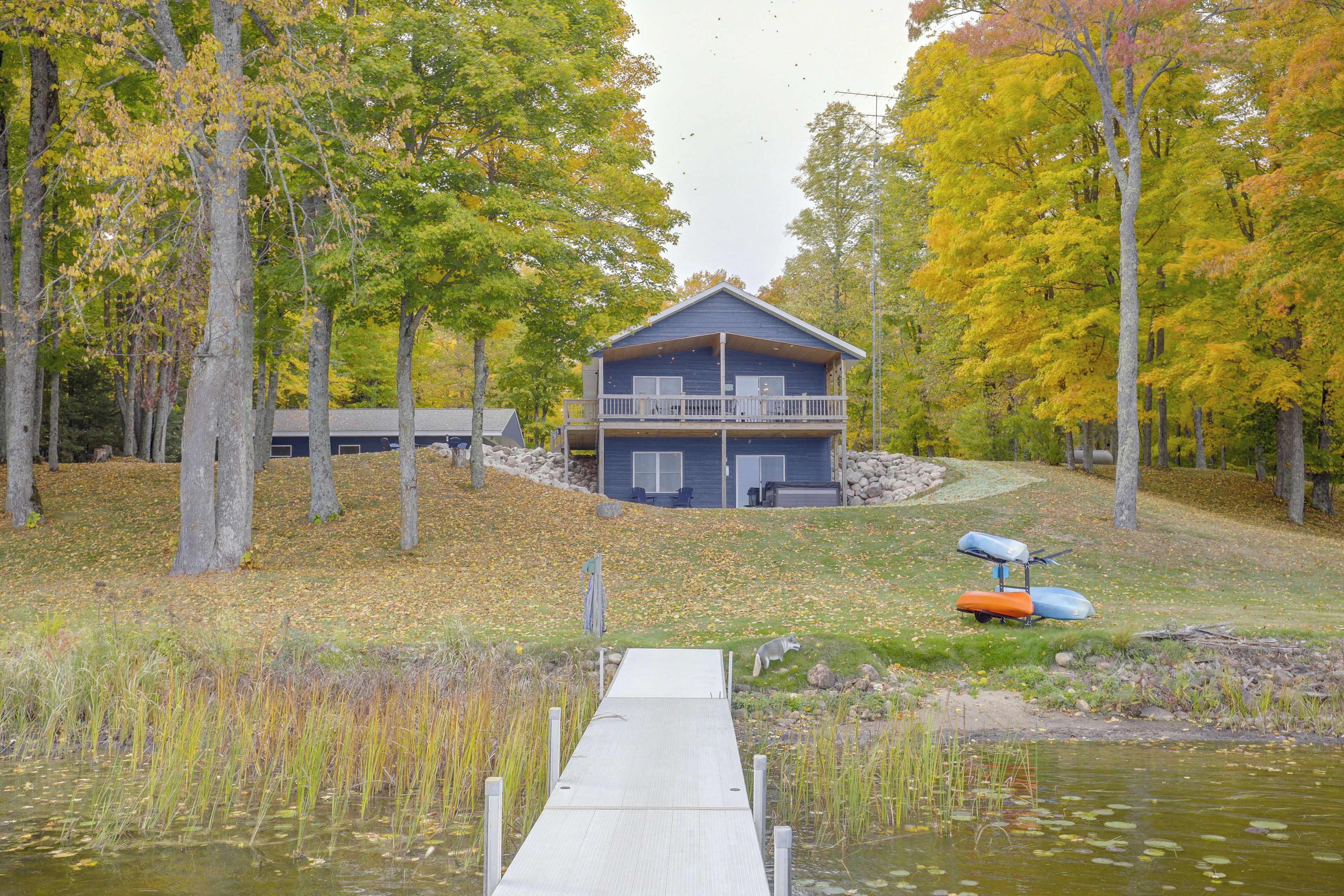 A lakeside cabin with a dock leading to the water, surrounded by trees and a grassy area.