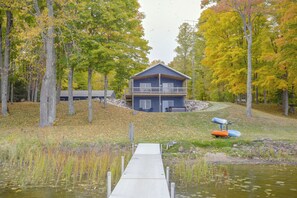 Un chalet au bord du lac, avec un quai donnant sur l’eau, entouré d’arbres et d’une zone herbeuse.