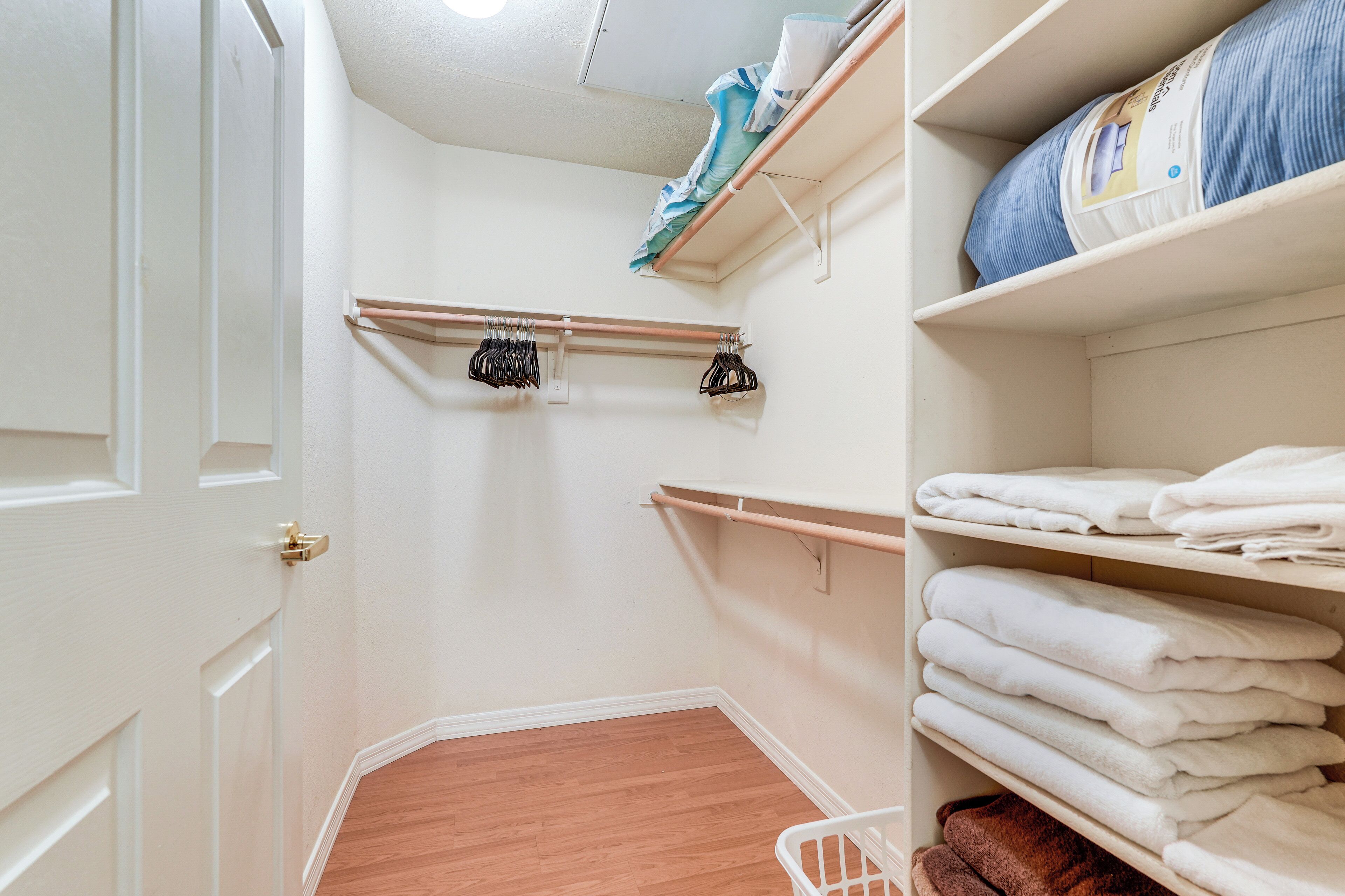 A walk-in closet with wooden flooring, a white door, and shelves with folded towels and a laundry basket.