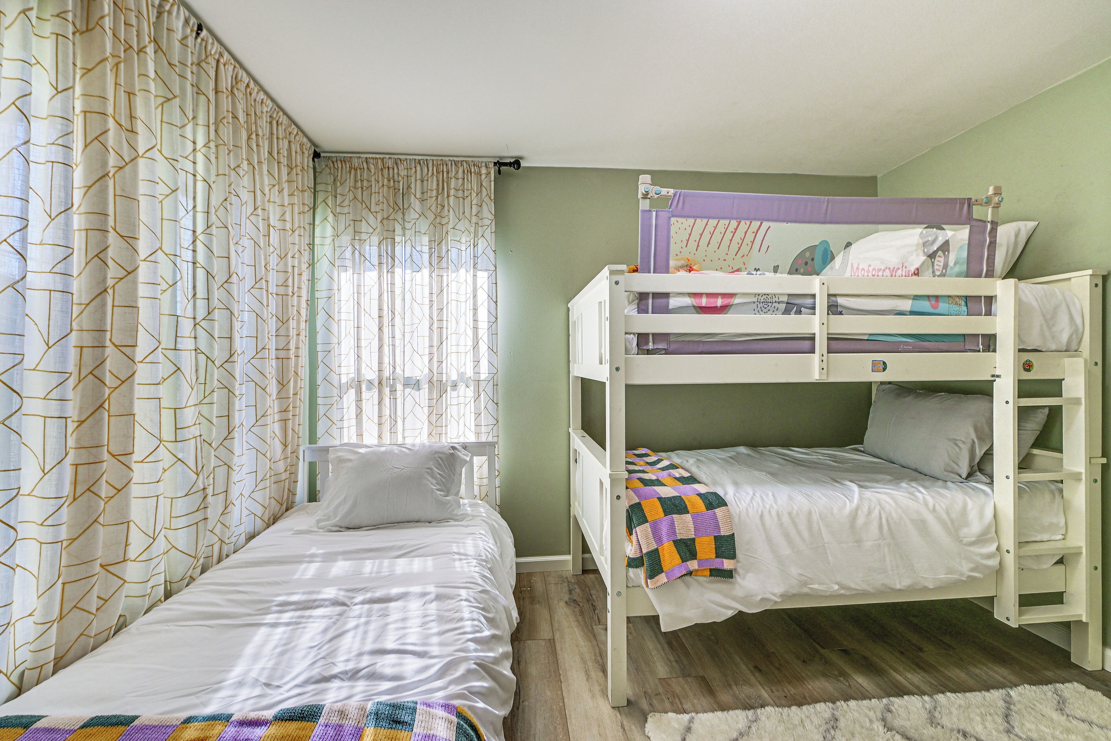 A room with a bunk bed, a single bed, and a window with curtains.