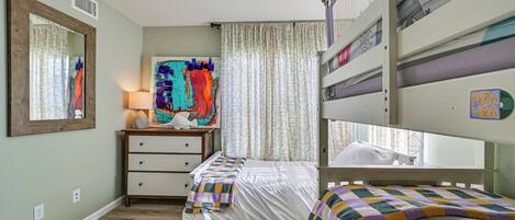 Un dormitorio con literas, una mesita de noche con lámpara, un aparador y un cuadro abstracto y colorido en la pared.