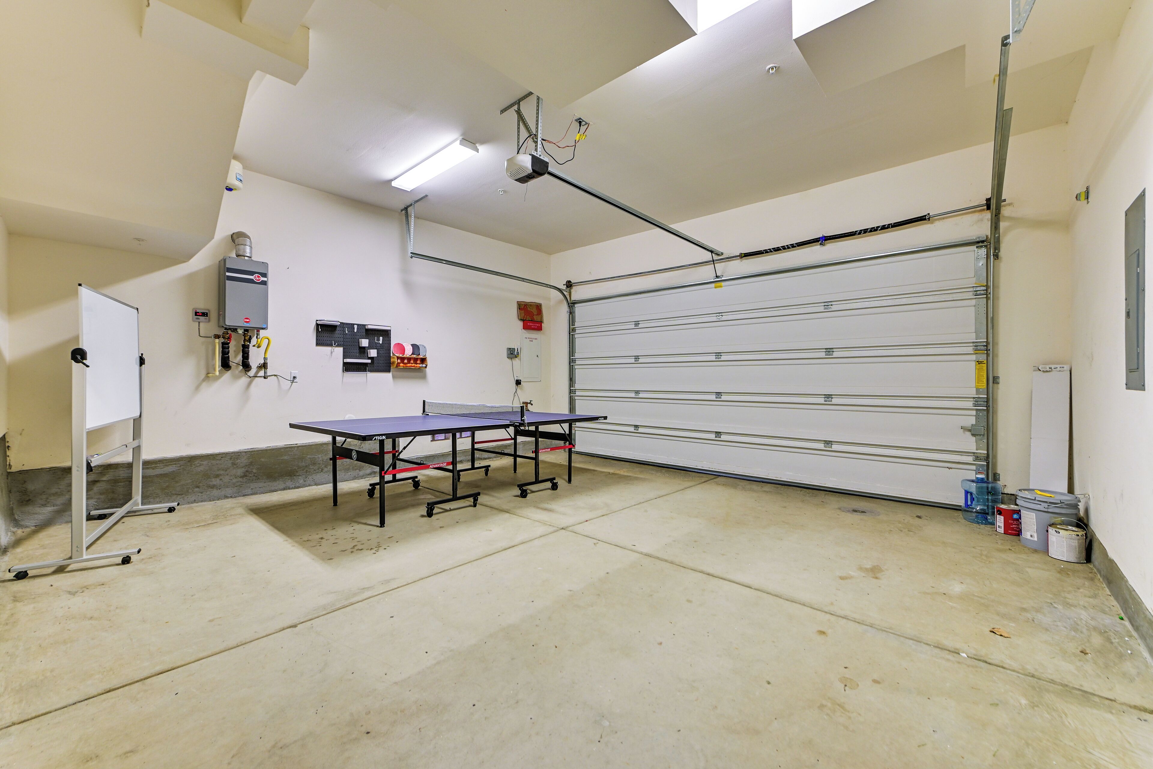 A spacious indoor area with a ping pong table, a whiteboard, and a garage door.
