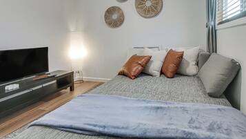 Une chambre moderne équipée d’un téléviseur à écran plat, d’une table de chevet, d’une lampe et d’un lit avec des oreillers.