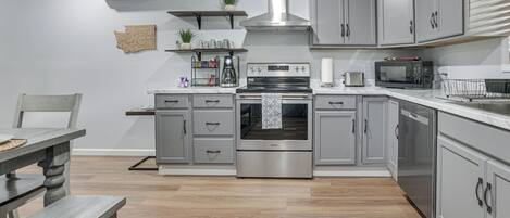 A modern kitchen with grey cabinets, a stainless steel range hood, a built-in oven, a microwave, and a coffee maker.