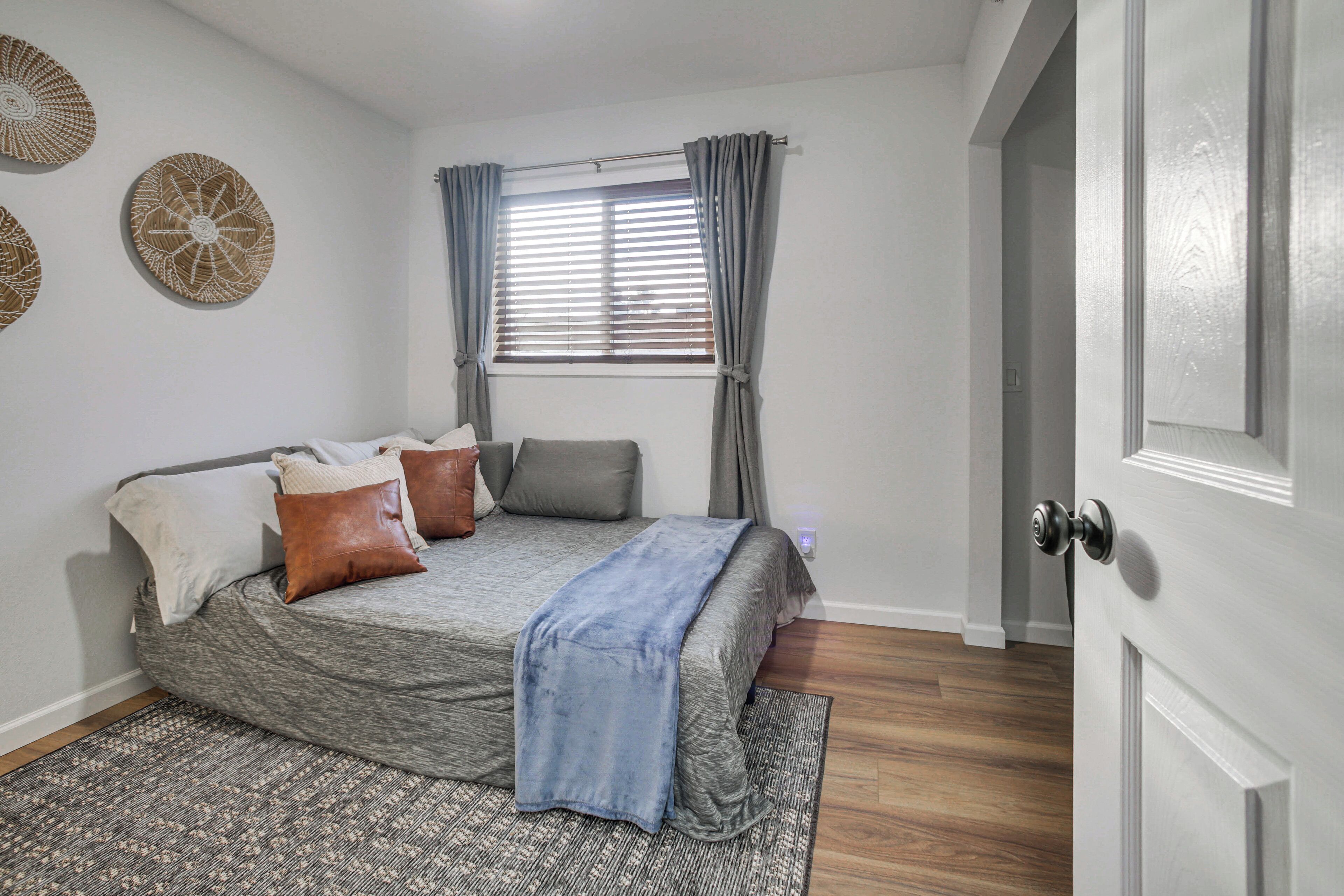 A bedroom with a bed, pillows, a window with curtains, a door, and a patterned rug.