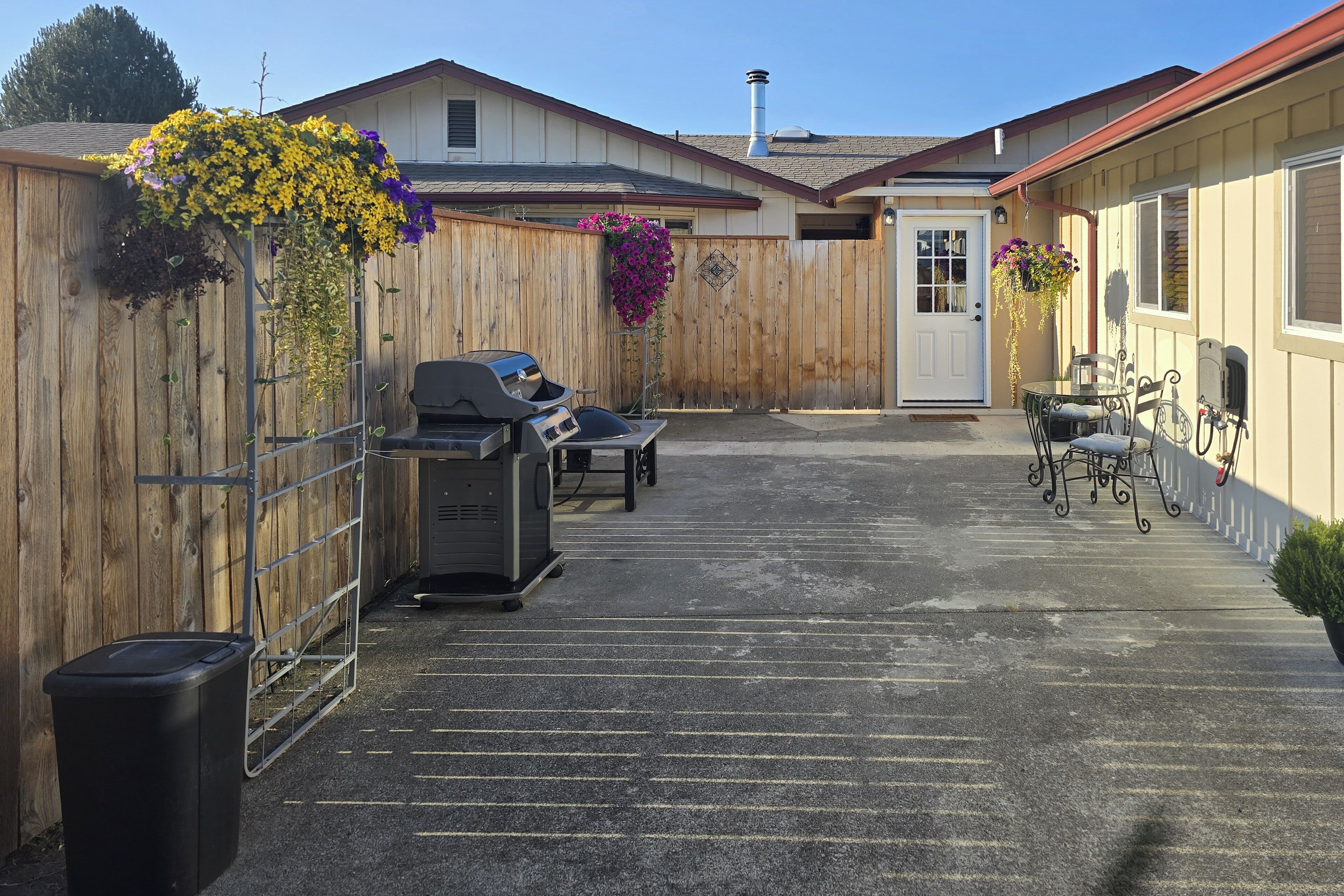 A covered outdoor patio with a barbecue grill, a trash bin, and a seating area with a table and chairs.