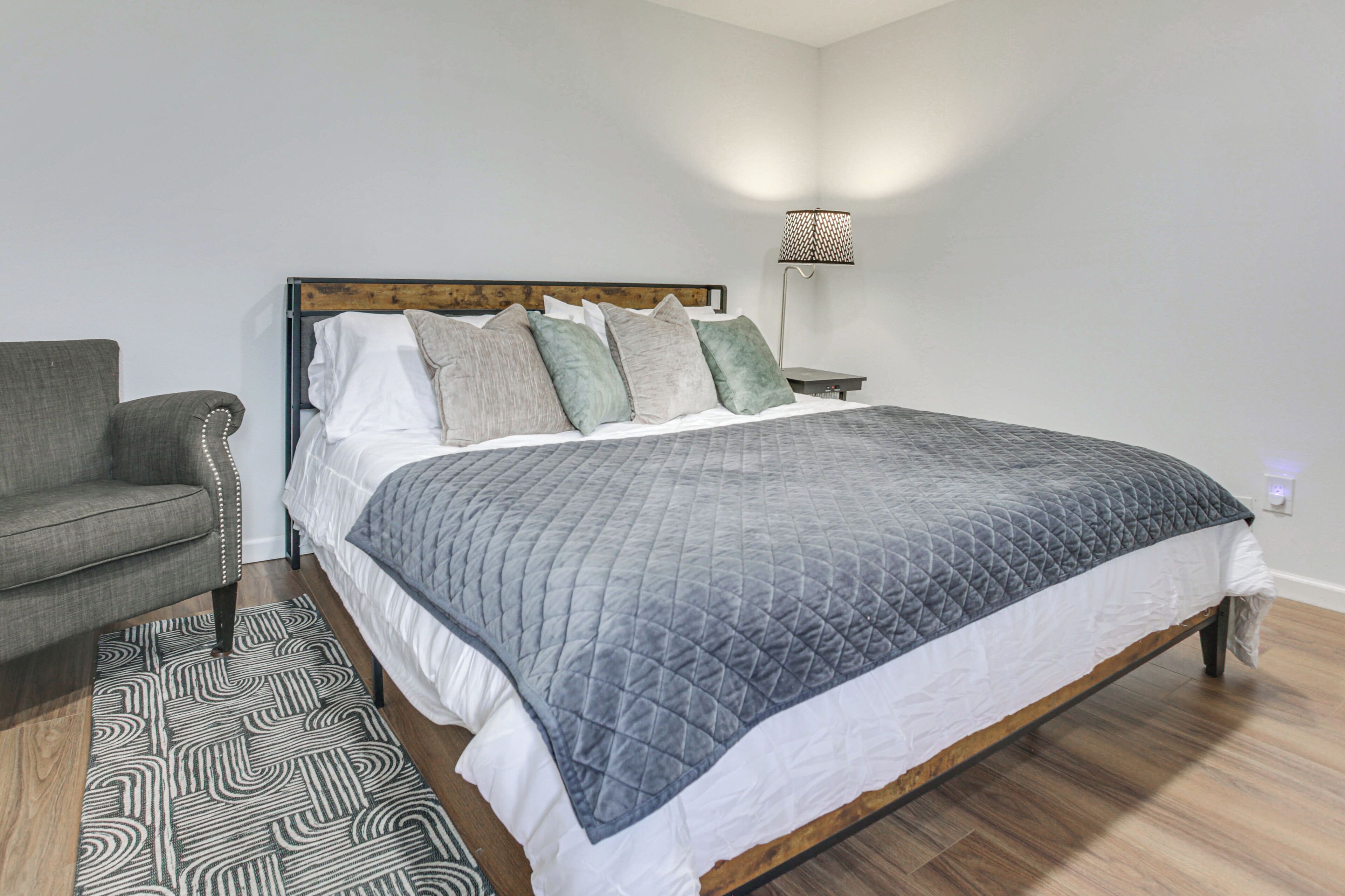 A bedroom with a bed, a chair, a nightstand, and a lamp.