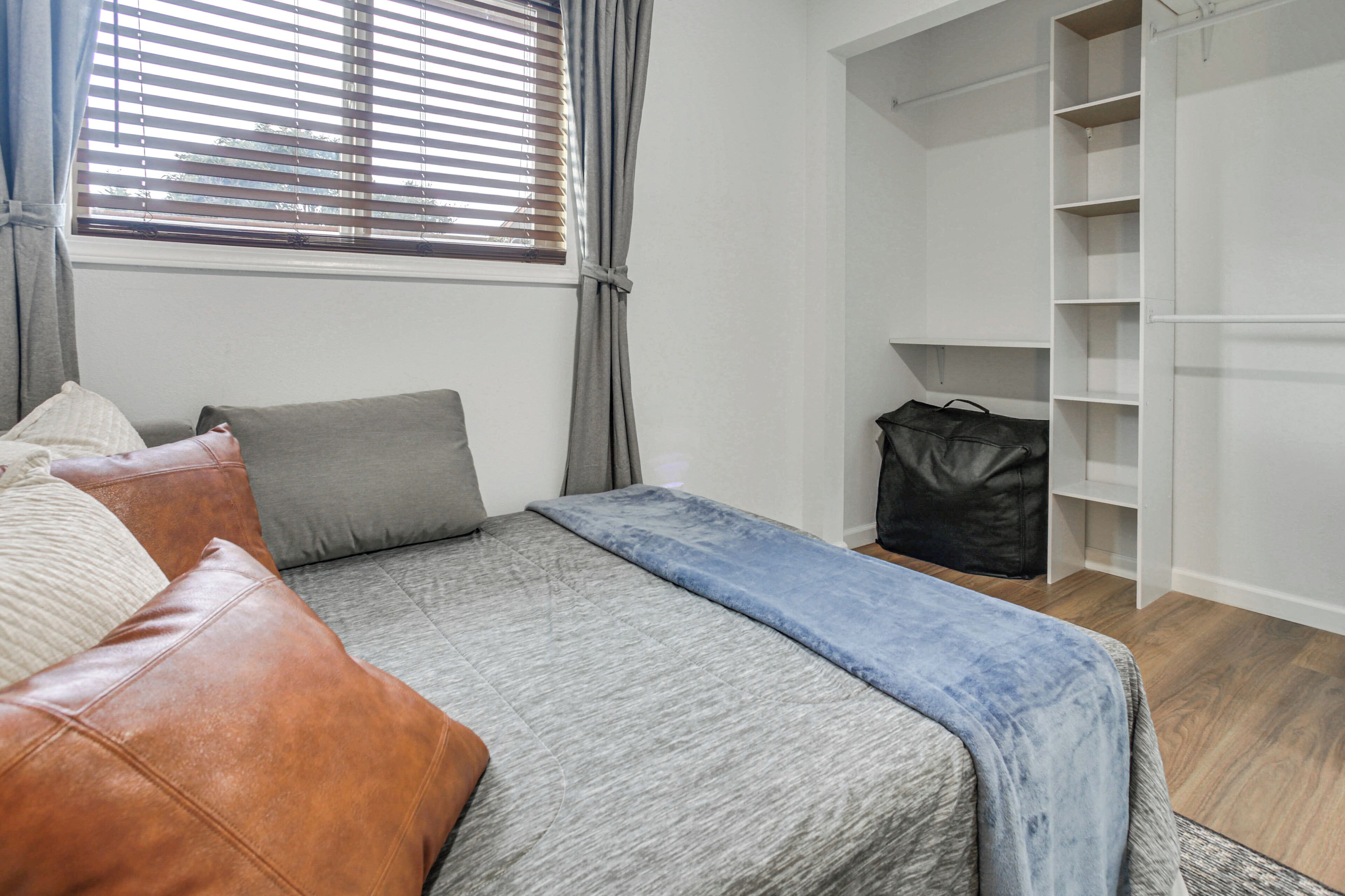 A bedroom with a bed, a wardrobe, and a window with blinds.