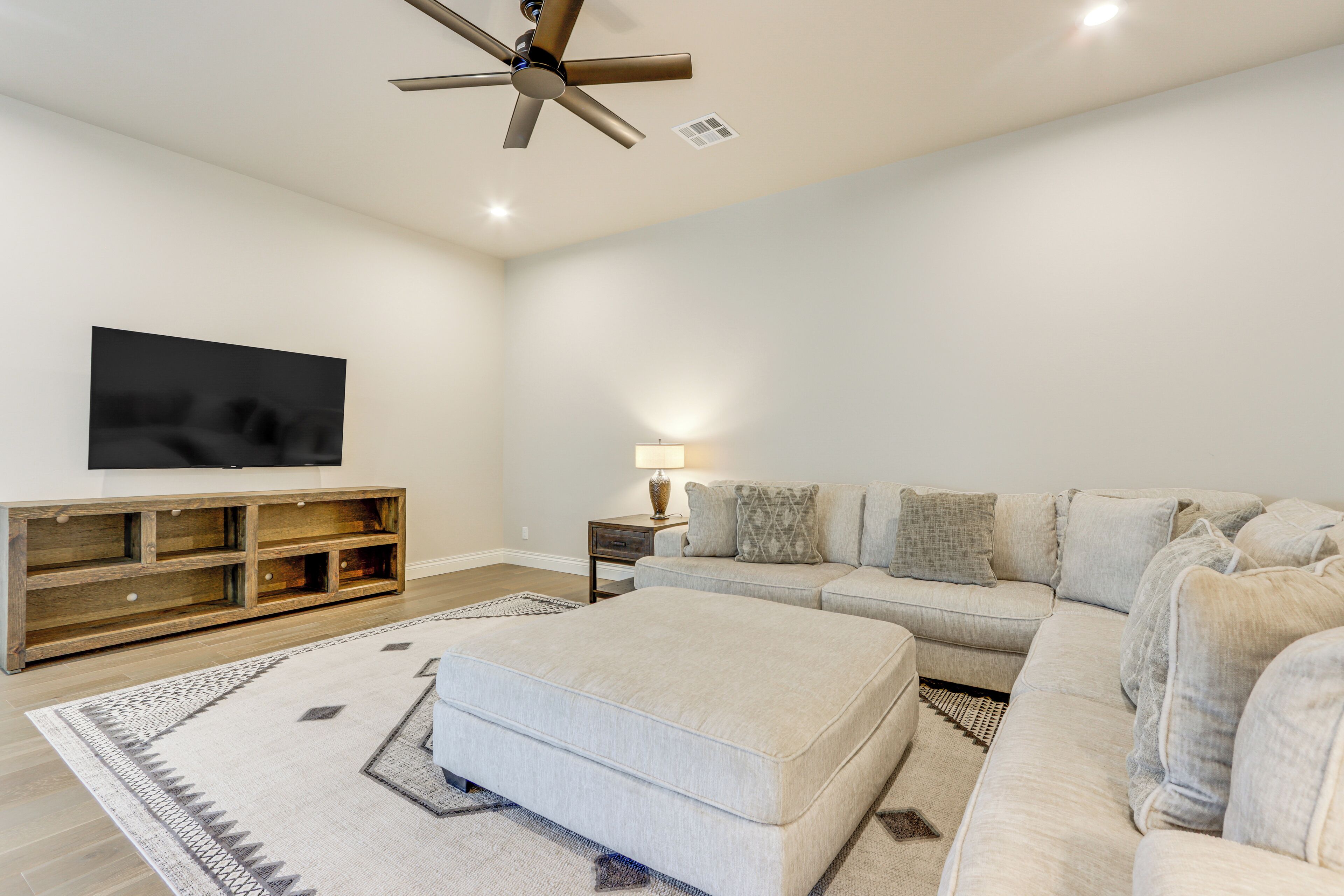 A modern living room with a sectional sofa, a flat-screen TV, a wooden entertainment unit, and a ceiling fan.