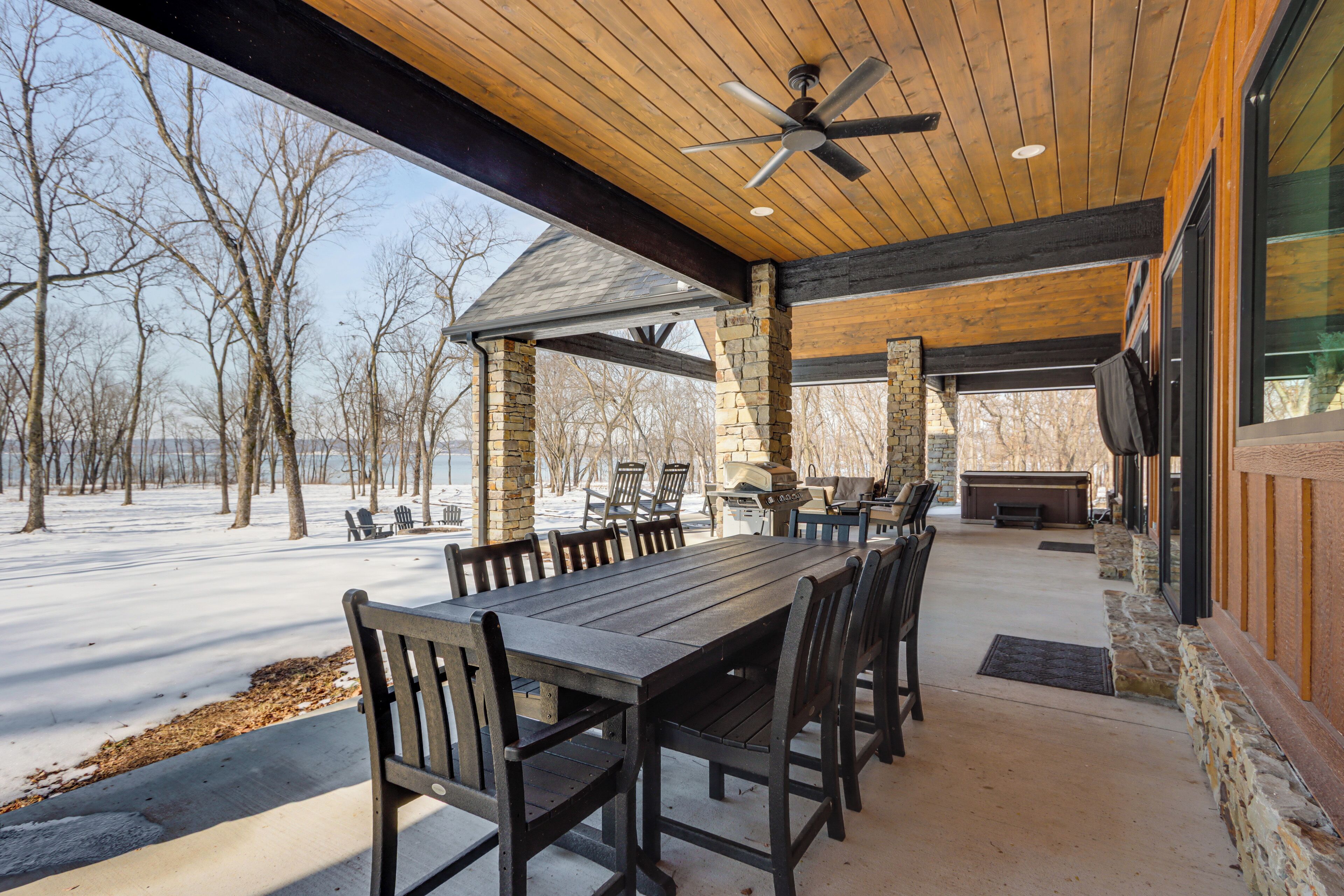 An outdoor covered patio with a wooden table and chairs, stone pillars, and a stone fireplace.