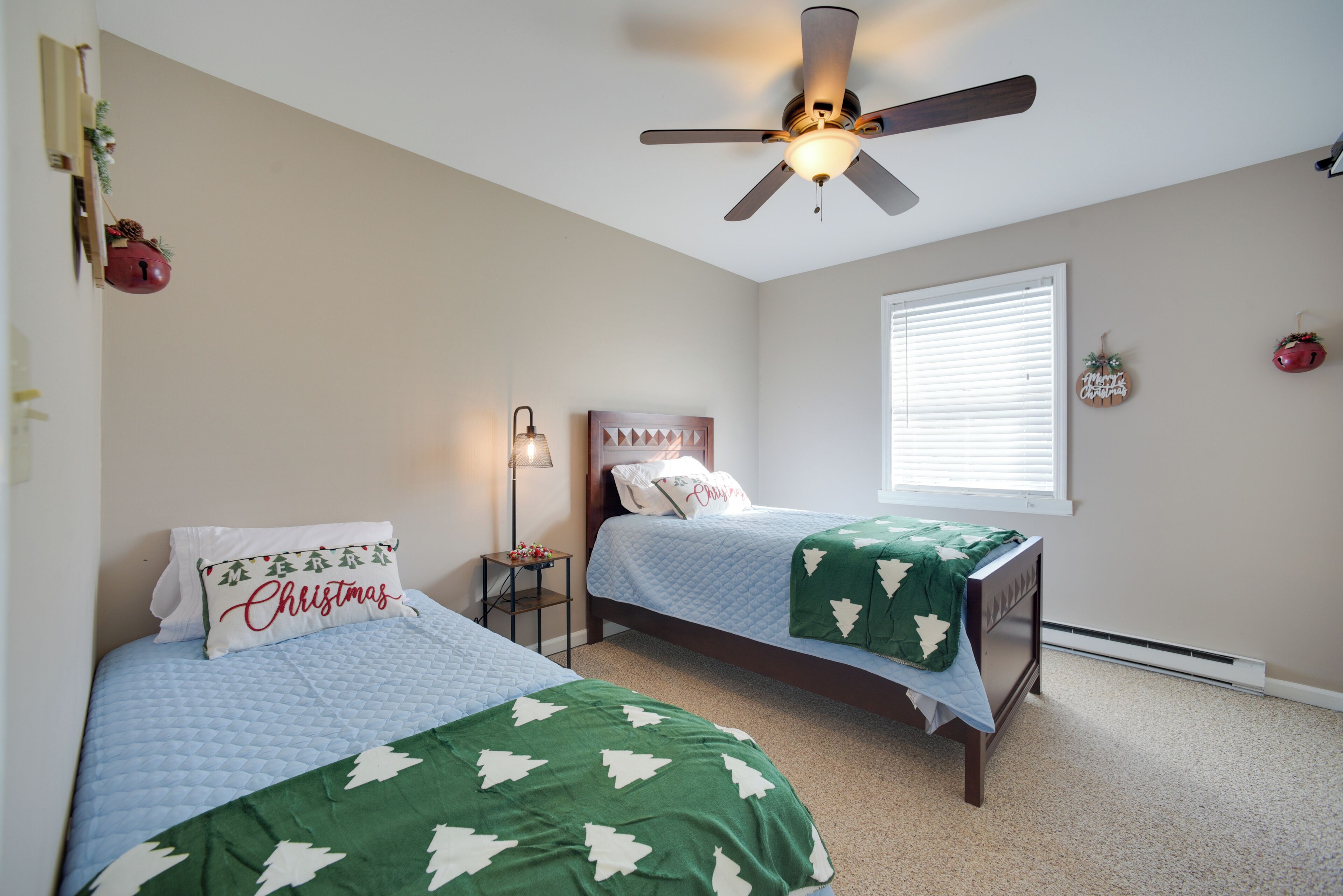 A bedroom with two beds, a ceiling fan, a nightstand, a lamp, and a window with blinds.
