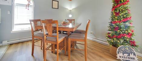 Uma área de refeições com uma mesa e cadeiras de madeira, uma árvore de Natal com luzes e enfeites, e um letreiro com a mensagem 'Welcome to Lake George'.