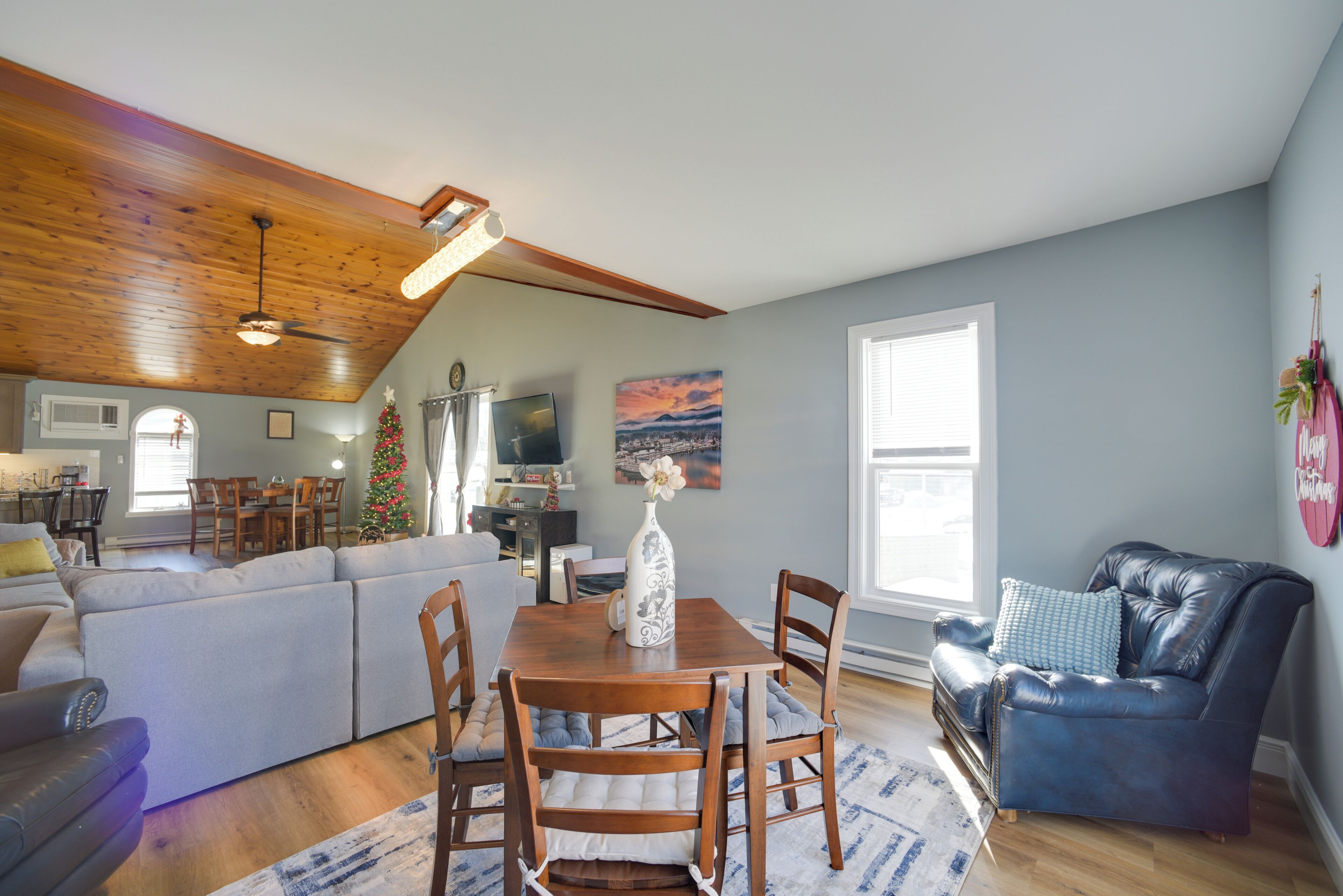 A spacious living area with a wooden ceiling, a dining table with chairs, a sofa, and a leather armchair.