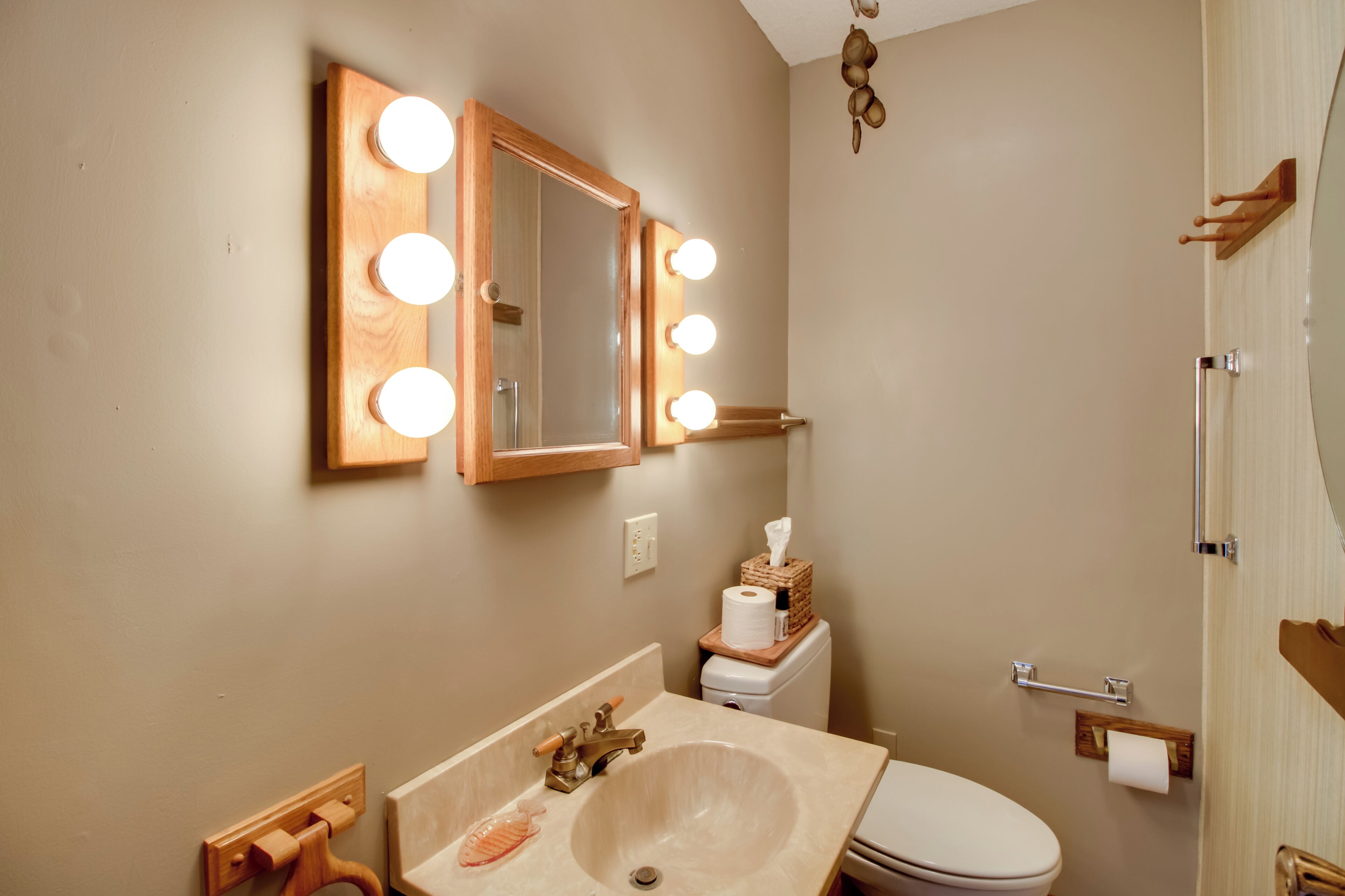 A bathroom with a vanity, sink, mirror with lights, toilet, and towel rack.