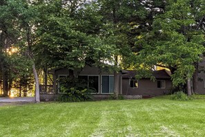 Une cabane dotée d’un porche, entourée d’arbres et bordée d’une pelouse.
