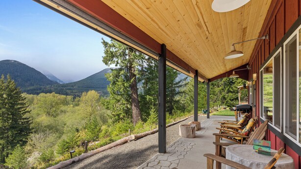 Un espacio al aire libre techado con sillas y una mesa de madera, con vistas a un paisaje montañoso.