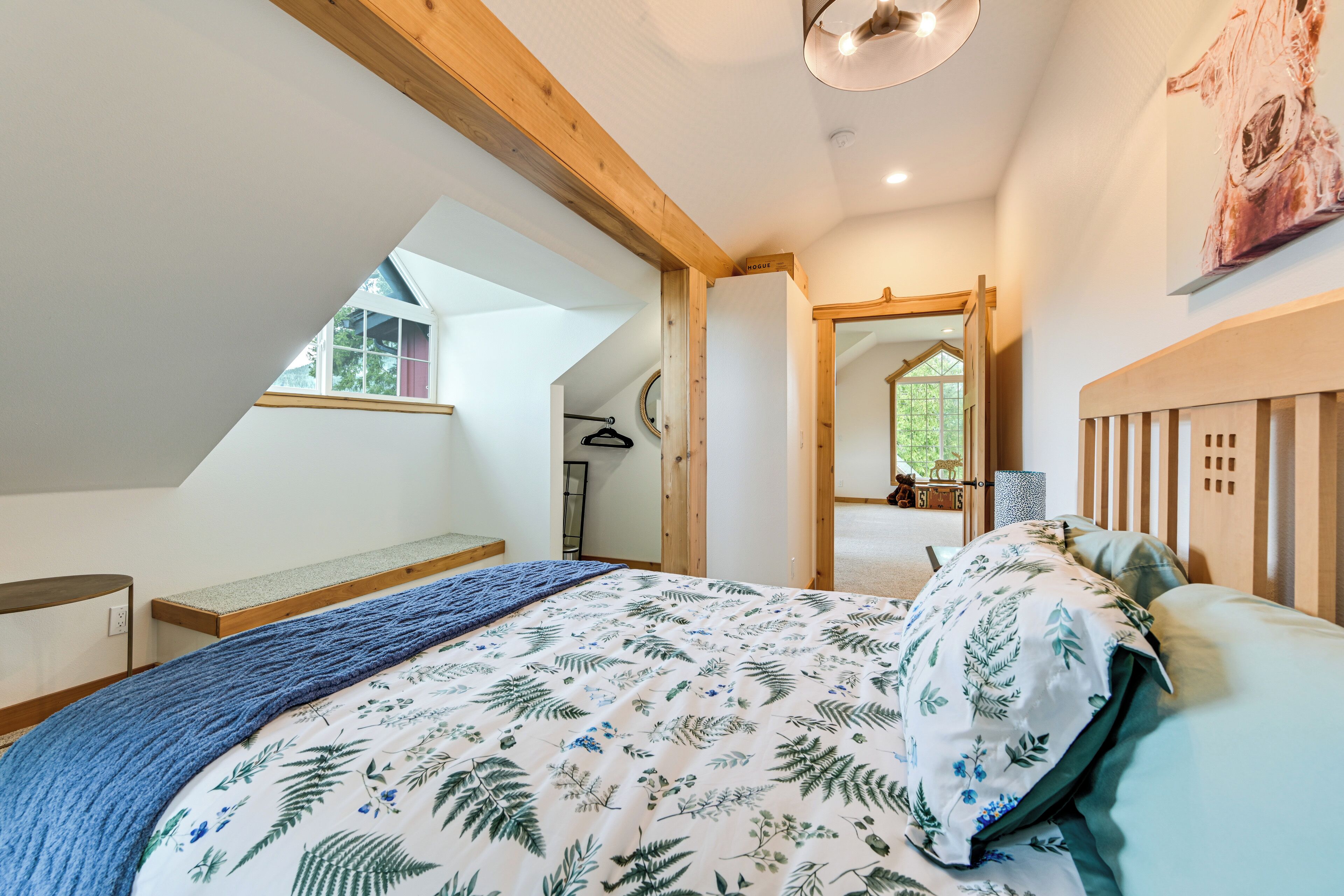 A bedroom with a sloped ceiling, a bed with a floral bedspread, a wooden headboard, and a large mirror on the wall.