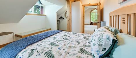 A bedroom with a sloped ceiling, a bed with a floral bedspread, a wooden headboard, and a large mirror on the wall.