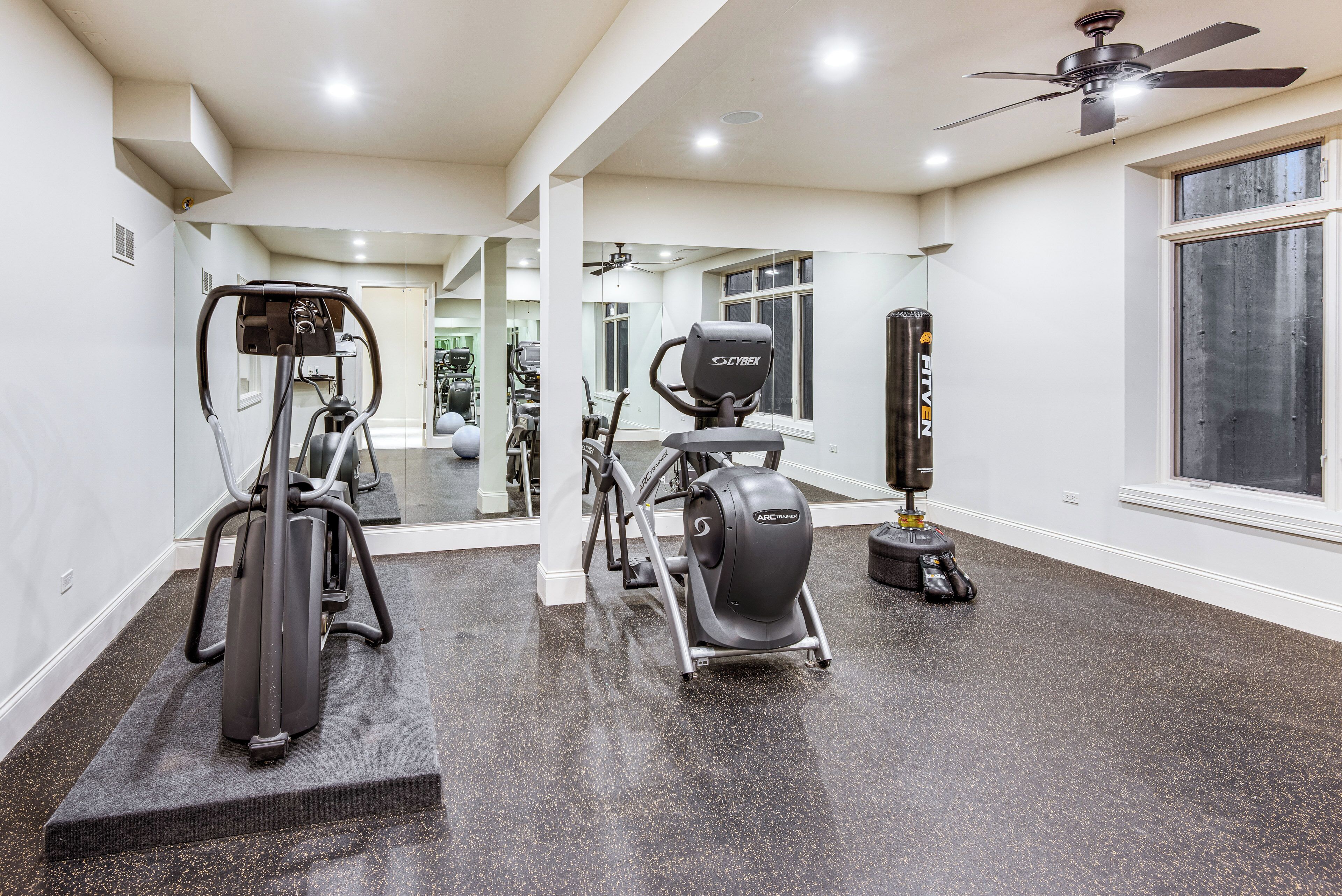 A home gym with cardio machines, a punching bag, and a ceiling fan.