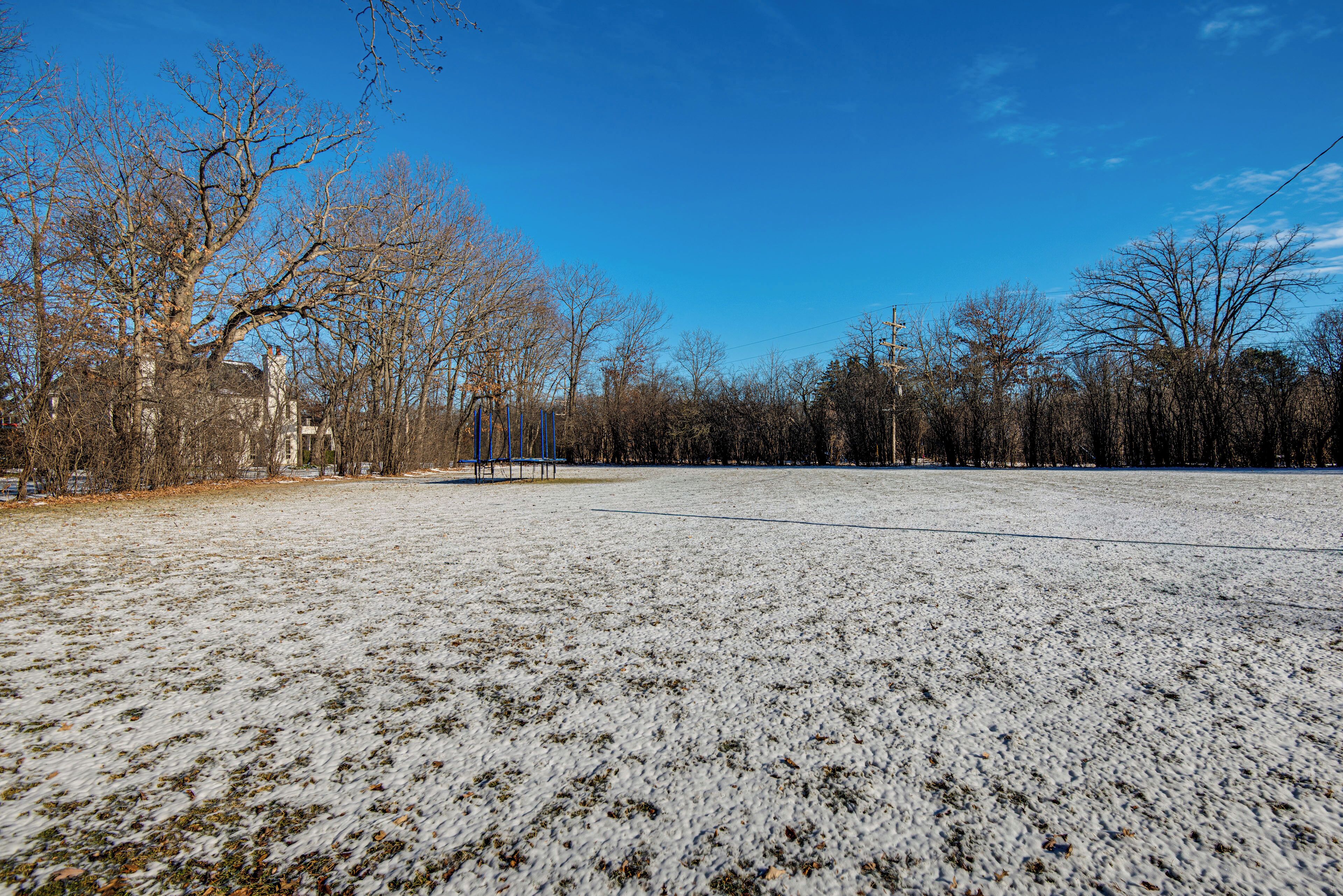 Ein schneebedecktes Feld mit kahl stehenden Bäumen und einem Gebäude in der Ferne.